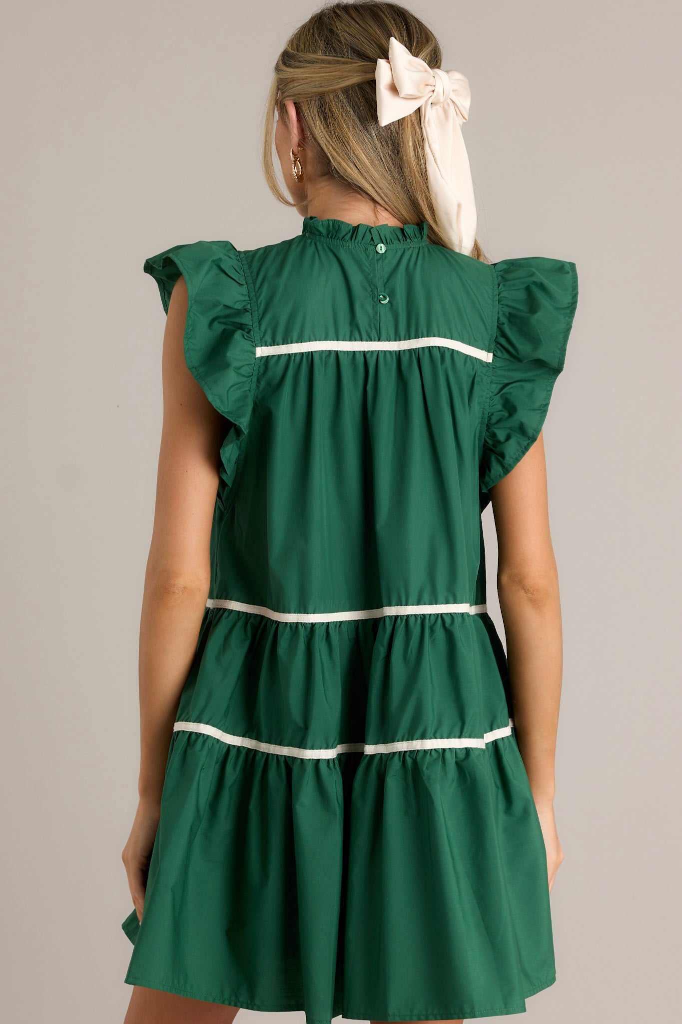 Back view of a green dress highlighting the ruffled sleeves and the round ruffle neckline.