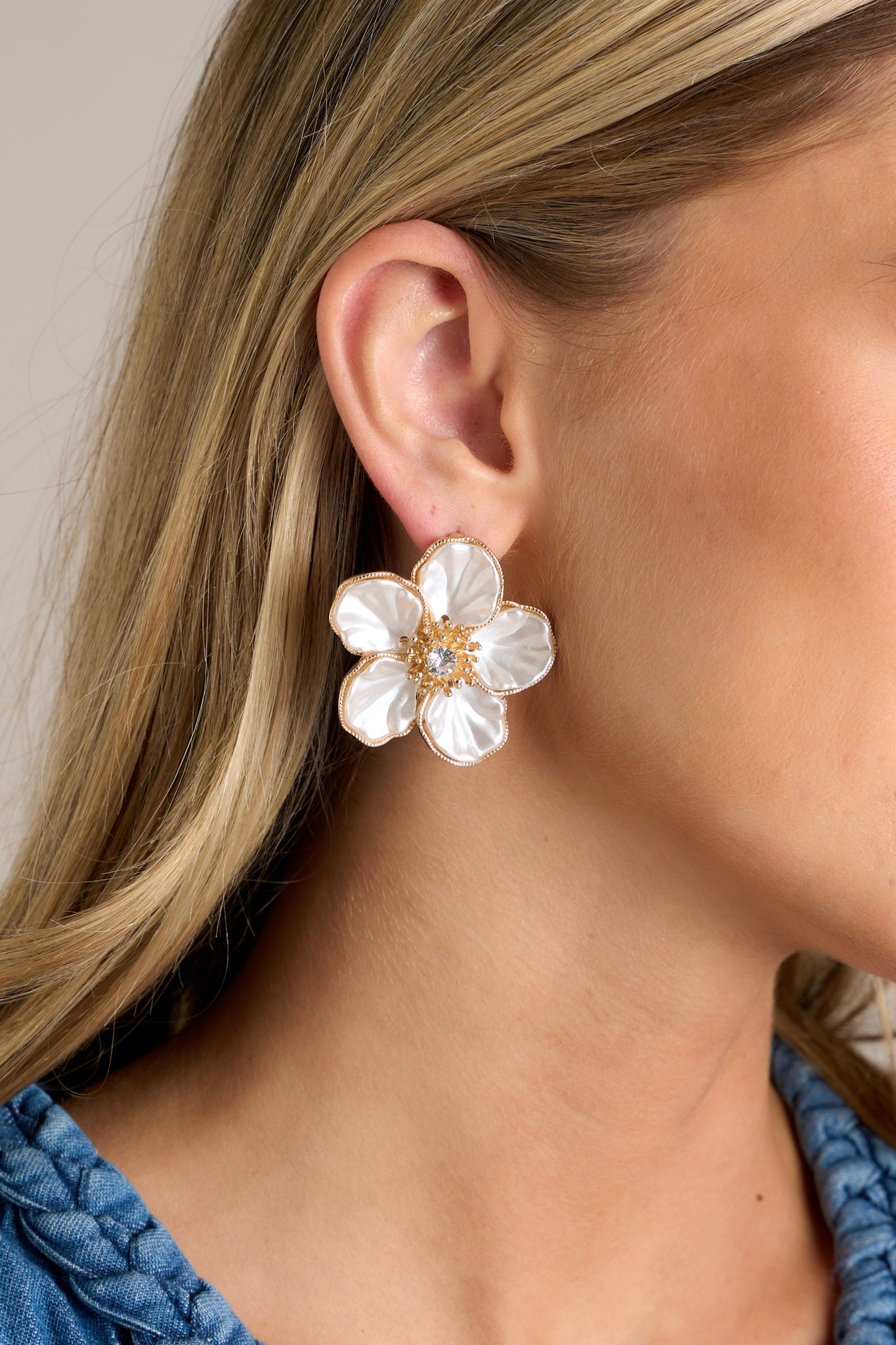 These ivory flower earrings feature gold hardware, a large statements flower with gold trim, a rhinestone in the middle with gold detailing, and secure post backings.