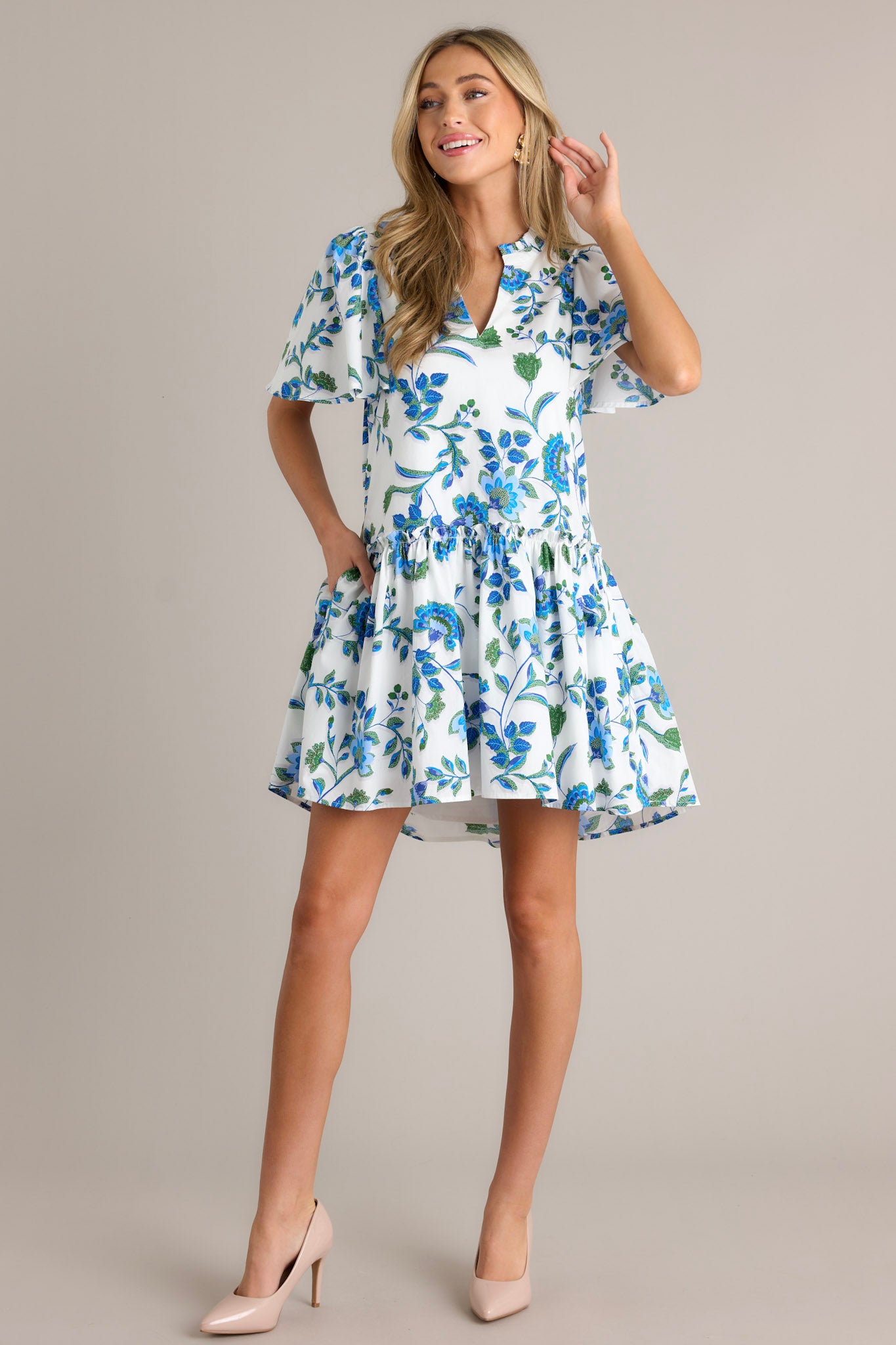 Full length view of a blue floral dress featuring a v-neckline, pleated detailing around the neck, a single tier, and short sleeves