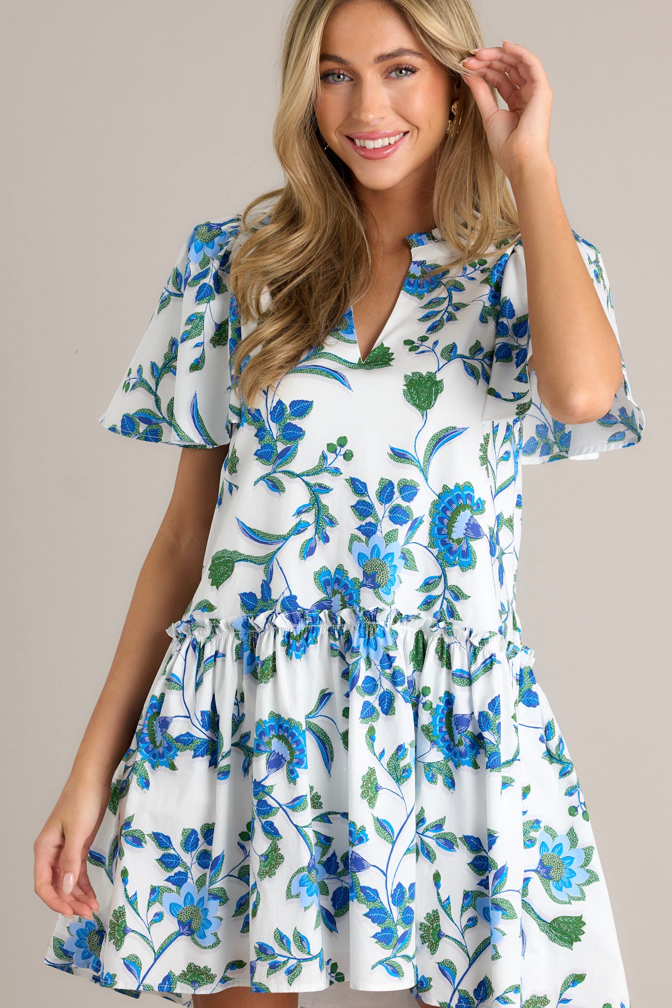 Front view of a blue floral dress featuring a v-neckline, pleated detailing around the neck, a single tier, and short sleeves.