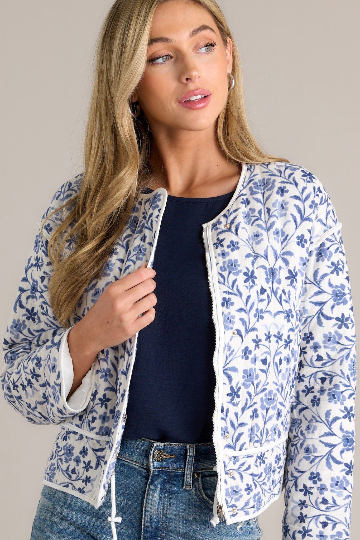 Front angled view of a blue jacket featuring a fun floral print, a round neckline, a hidden zipper, and front buttons