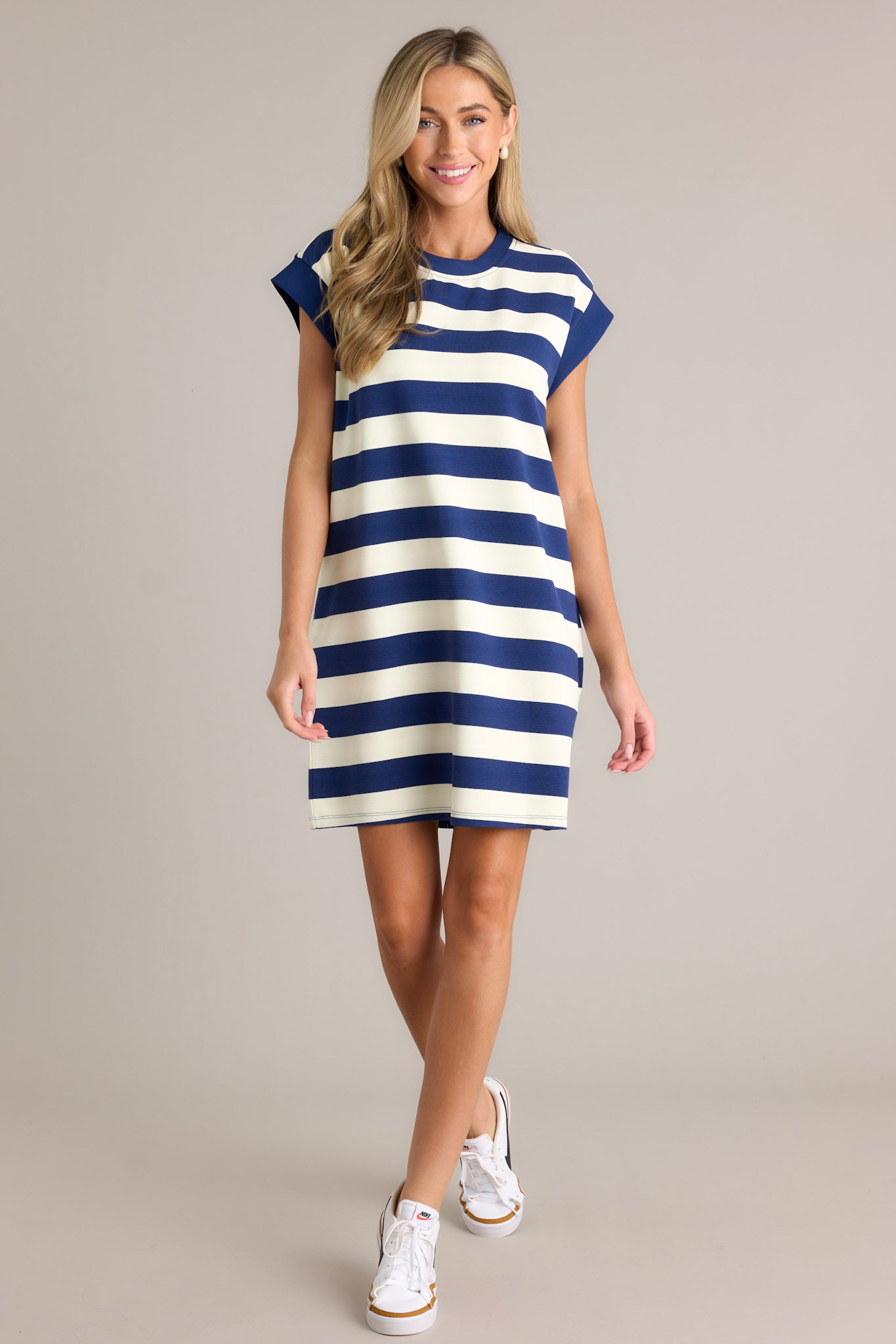 This navy stripe mini dress features a crew neckline, wide cap sleeves, functional hip pockets, and a relaxed fit.