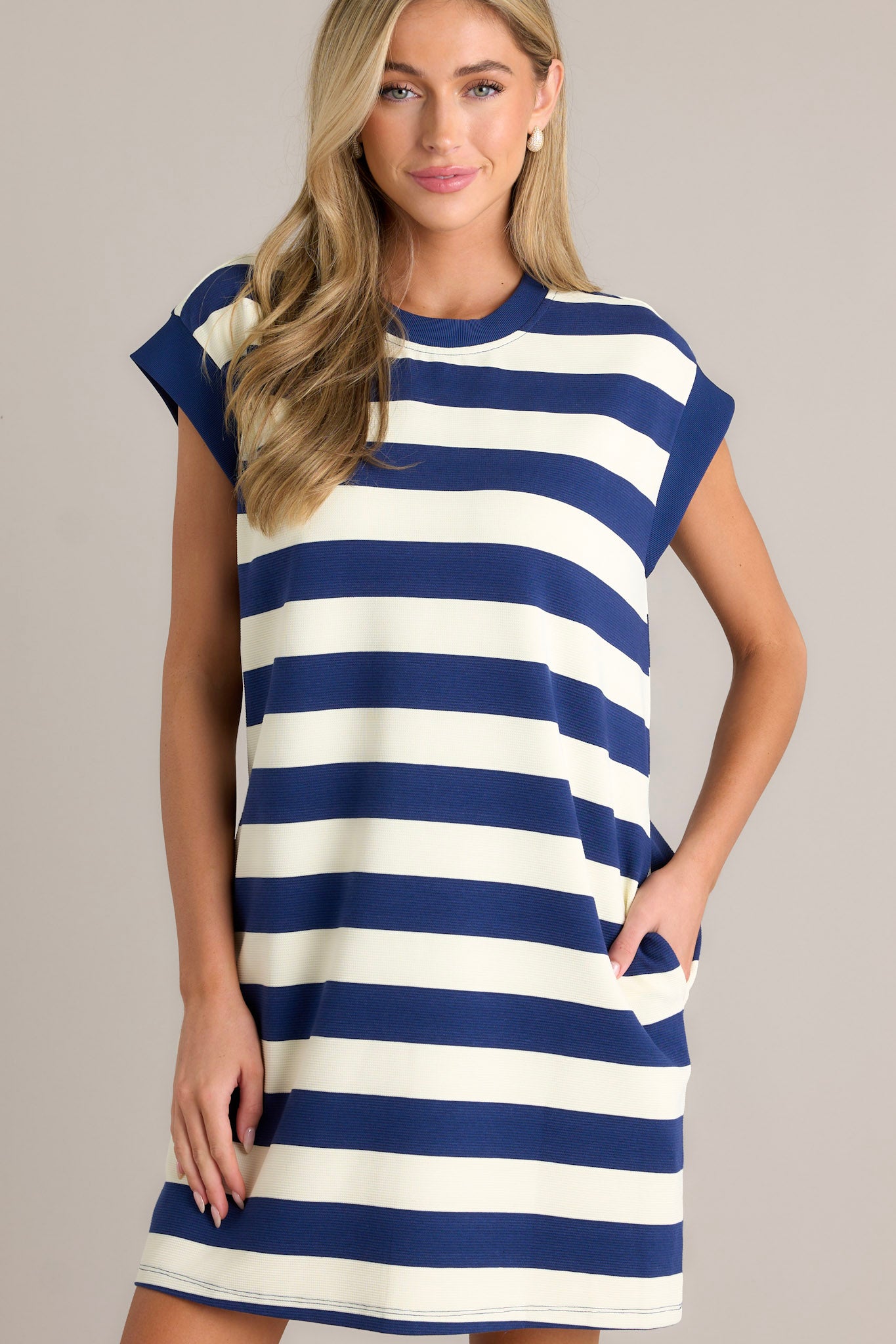 Angled front view of this navy stripe mini dress that features a crew neckline, wide cap sleeves, functional hip pockets, and a relaxed fit.