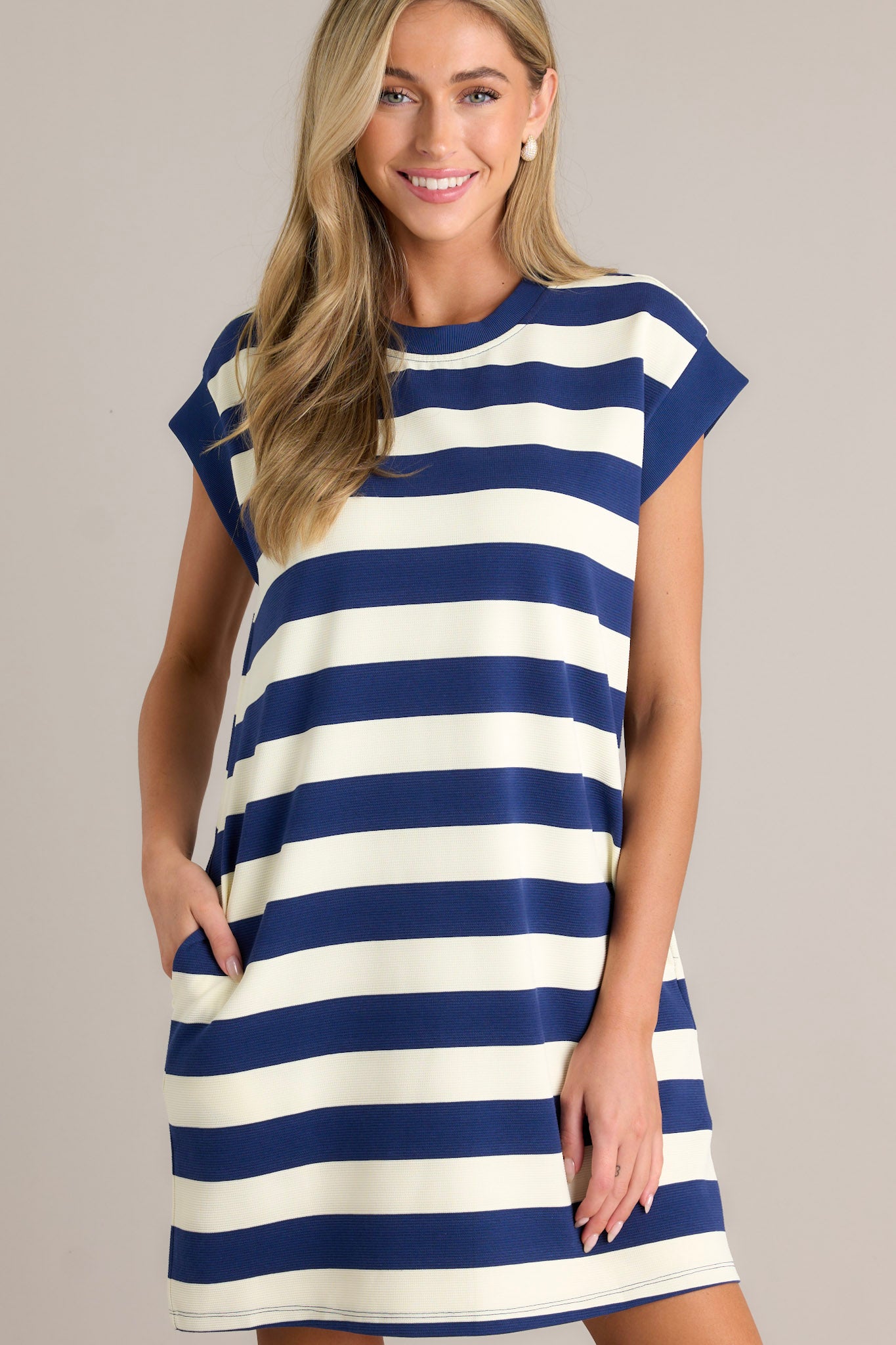 Front view of this navy stripe mini dress that features a crew neckline, wide cap sleeves, functional hip pockets, and a relaxed fit.