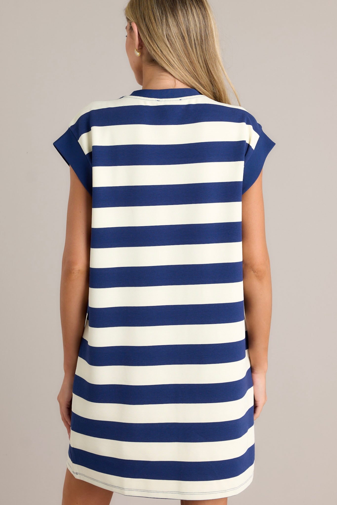 Back view of this navy stripe mini dress that features a crew neckline, wide cap sleeves, functional hip pockets, and a relaxed fit.