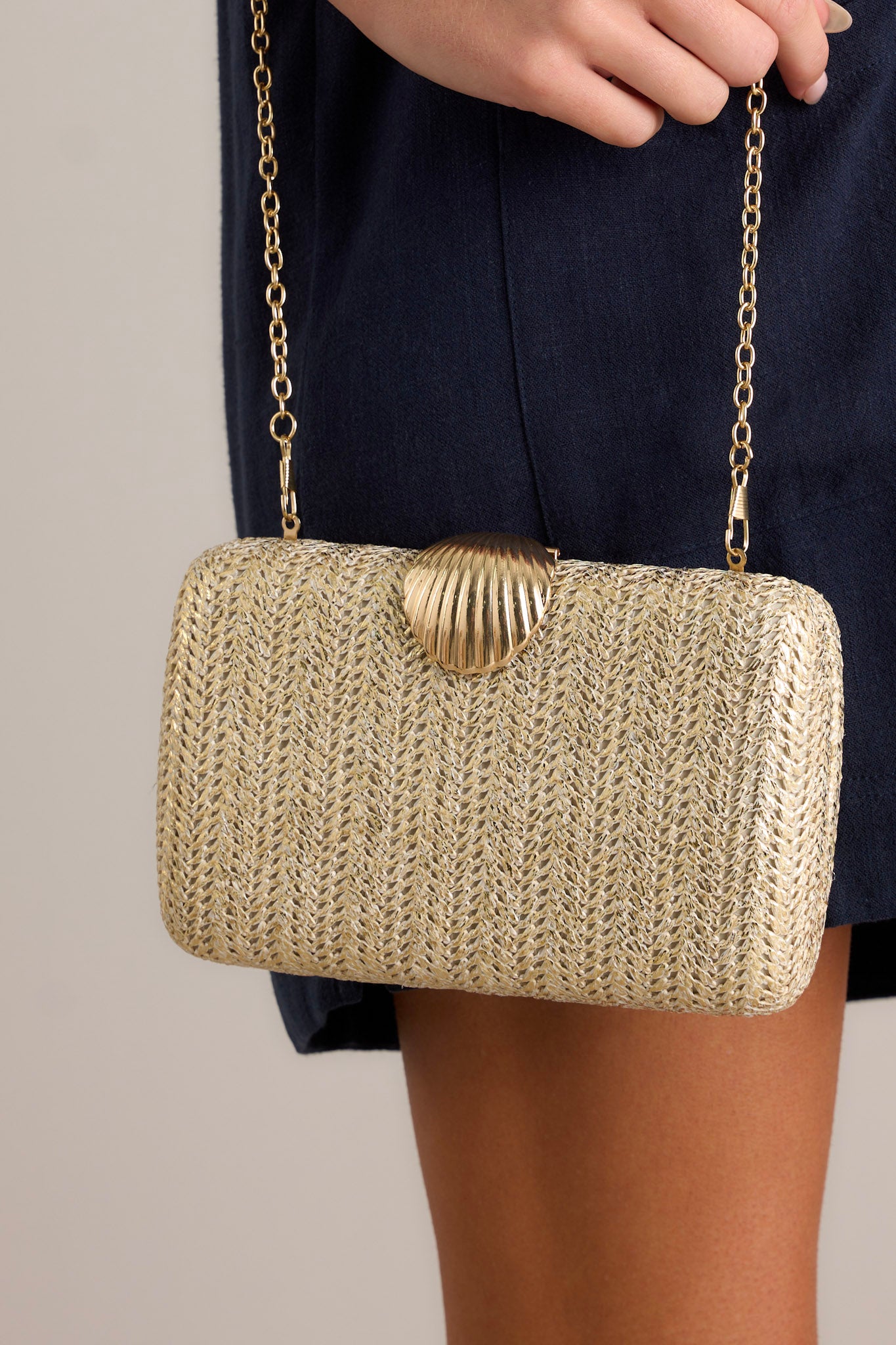 Close-up view of this gold woven clutch featuring a seashell snap closure, gold hardware, and an optional crossbody chain.&nbsp;