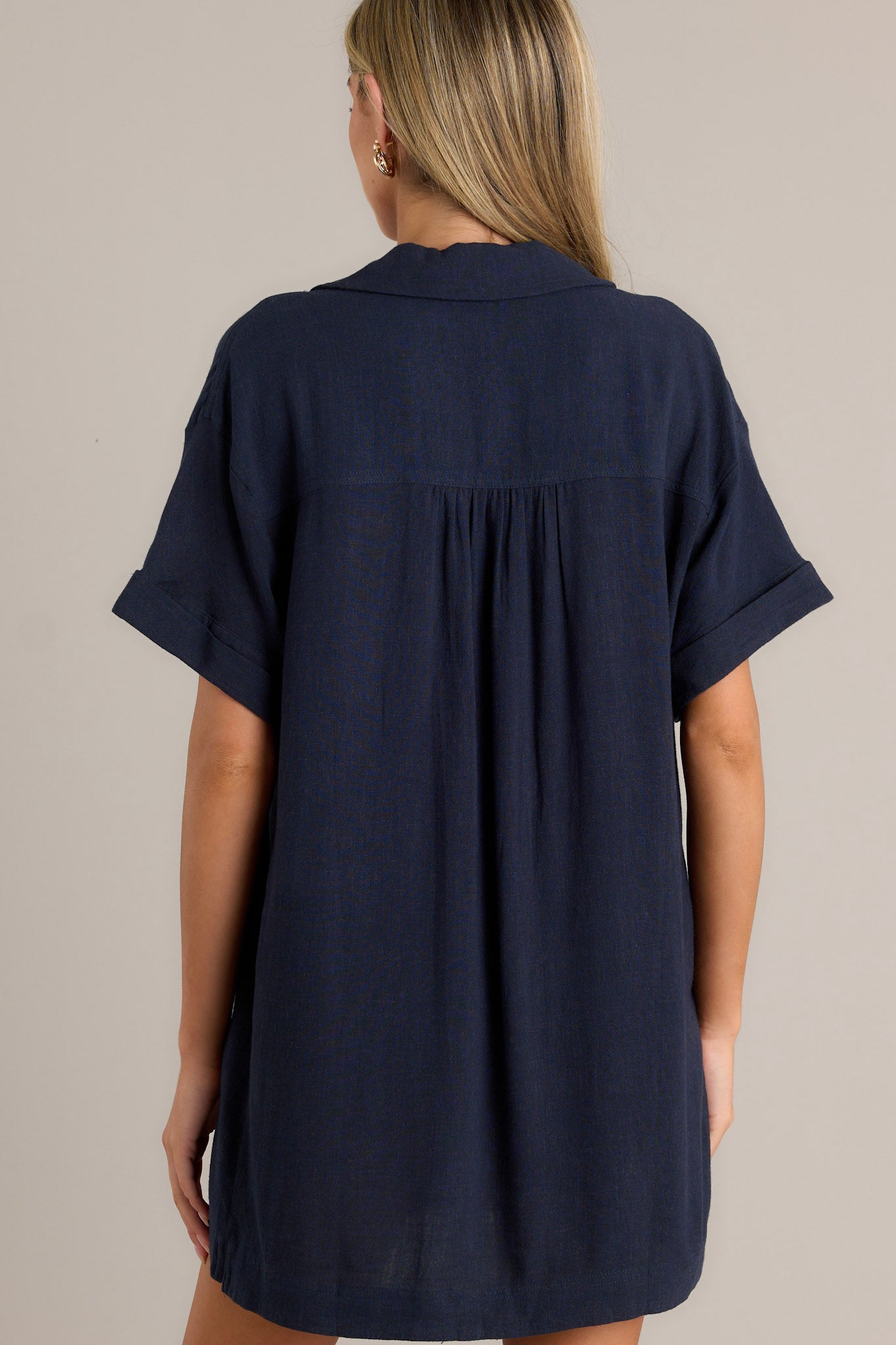 Back view of this navy dress that features a collared neckline, functional button front, functional pockets, short cuffed sleeves and a relaxed fit.