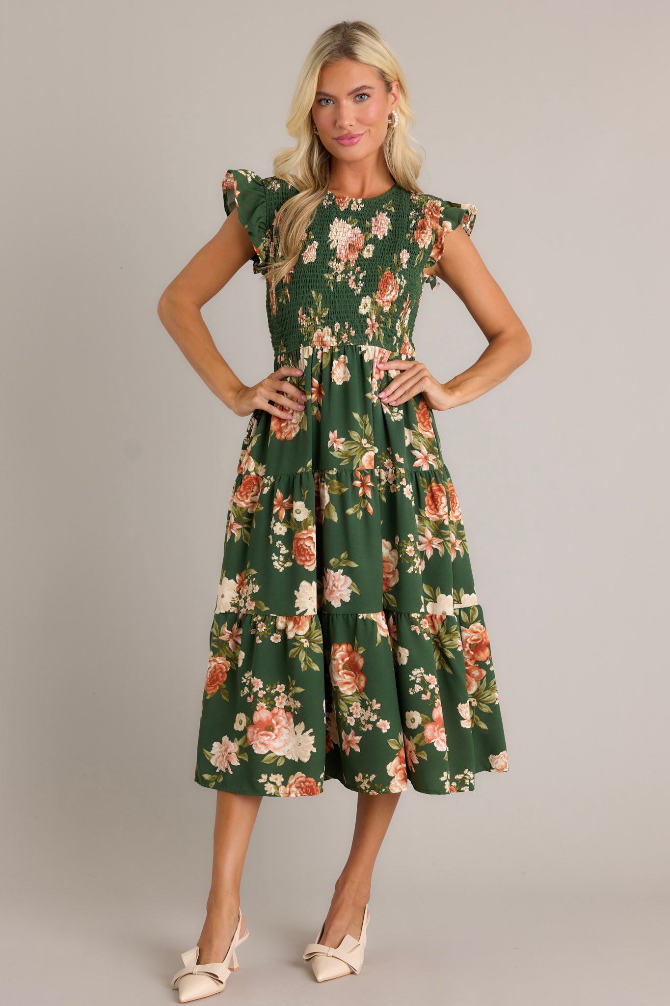 This green dress features a high neckline, a fully smocked bodice, a tiered design, short ruffle sleeves, a back button and loop closure and a flowing silhouette.