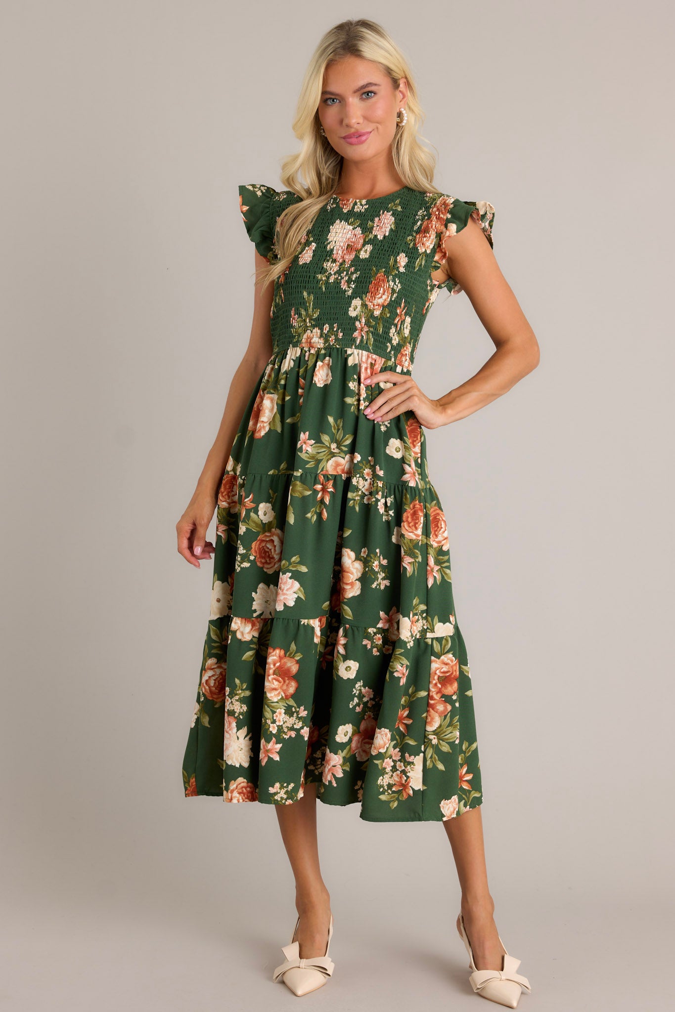 Full length view of a green dress with a high neckline, fully smocked bodice, tiered design, short ruffle sleeves, a back button and loop closure, and a flowing silhouette