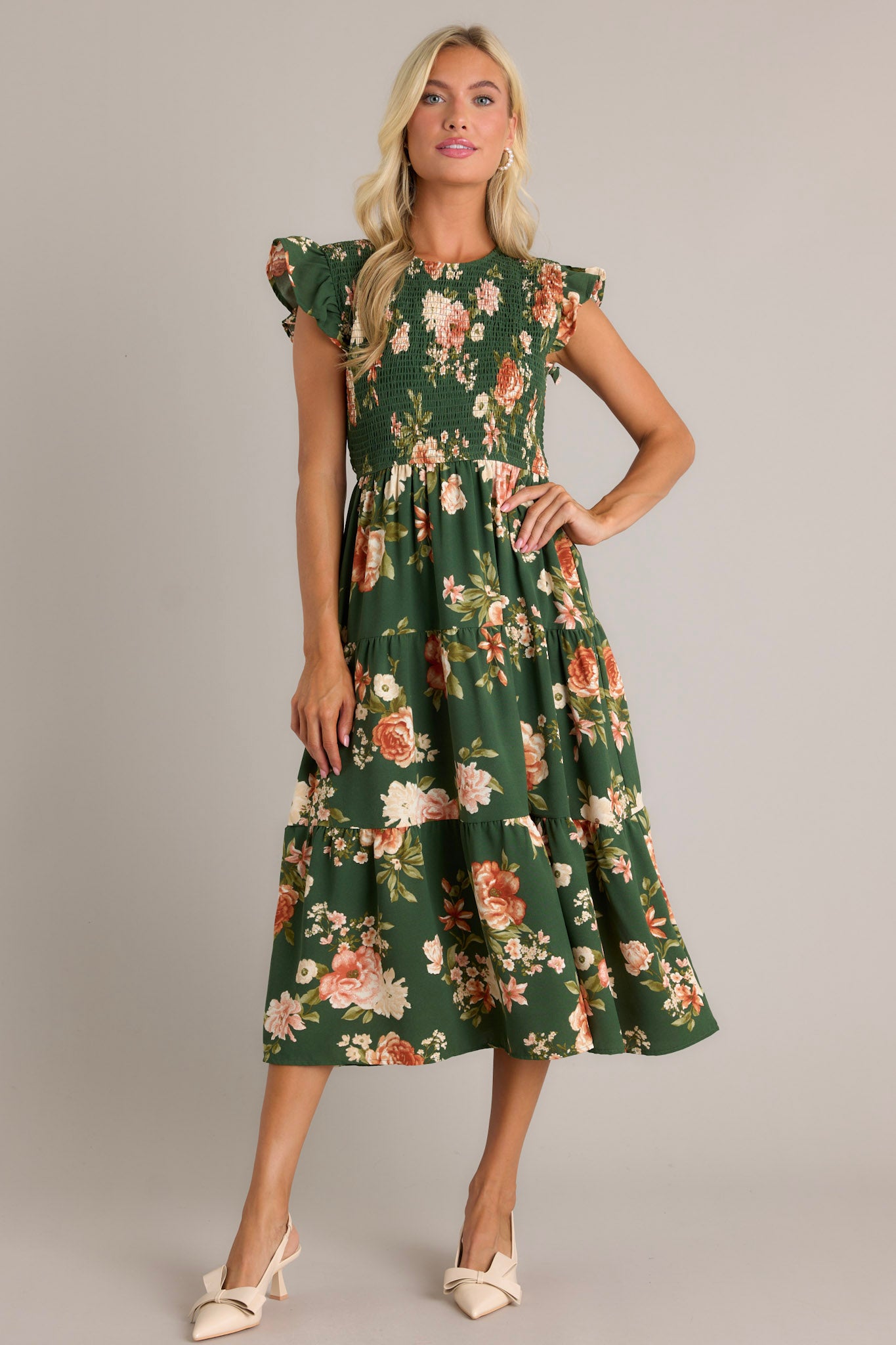 Full view of a green dress with a high neckline, fully smocked bodice, tiered design, short ruffle sleeves, a back button and loop closure, and a flowing silhouette