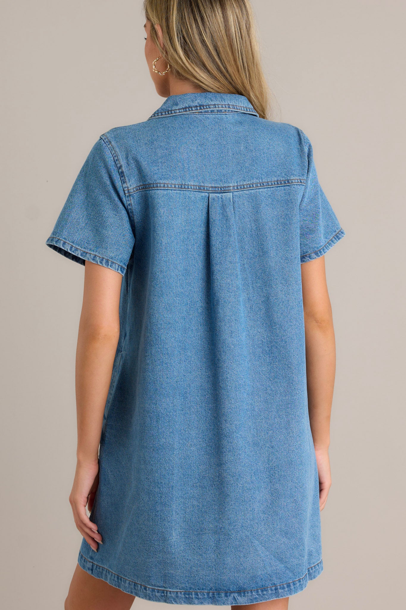 Back view of the denim mini dress highlighting the back seam details, the continuation of the functional bust pockets, and the short sleeves.