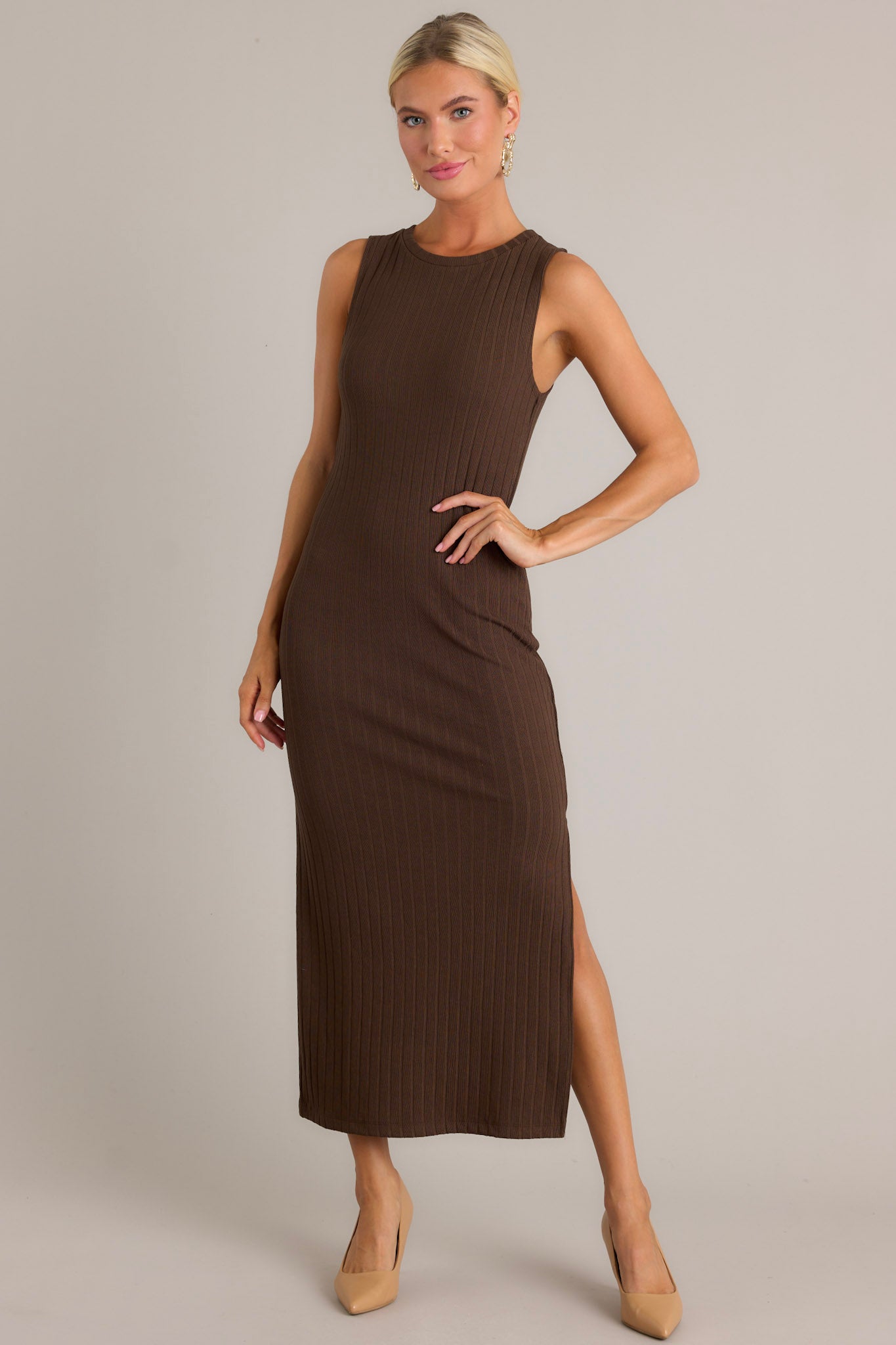 Full length view of a brown dress featuring a high rounded neckline, soft ribbed fabric, a bodycon fit, a slit in the left leg, and a sleeveless design