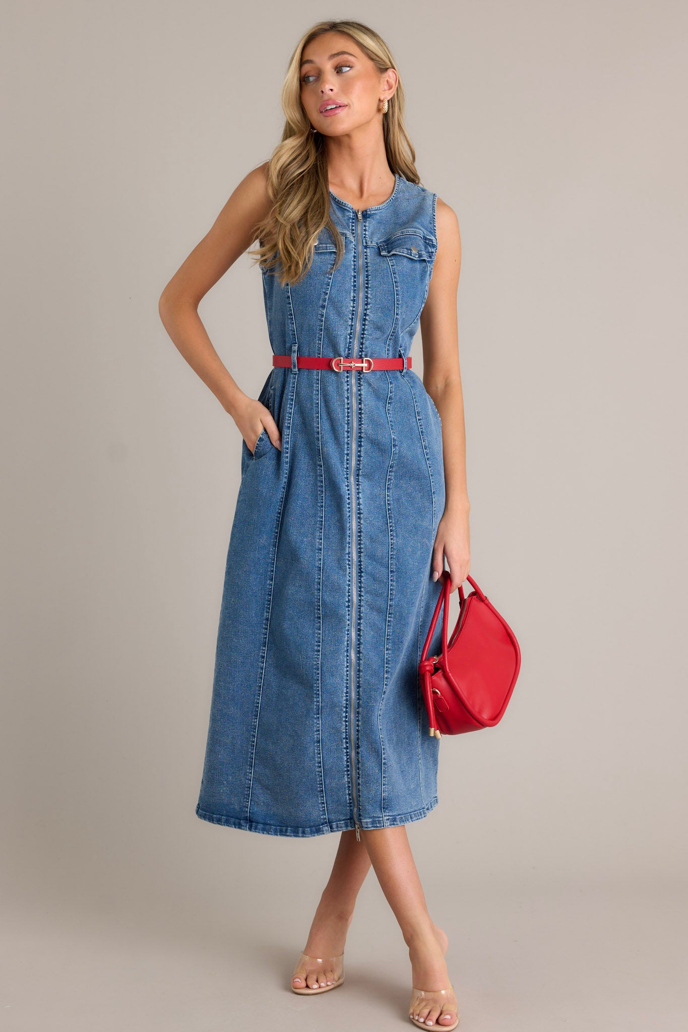 This denim dress features rounded neckline, a functional front zipper, faux chest pockets, functional hip pockets, a self-tie denim drawstring belt and a sleeveless design.