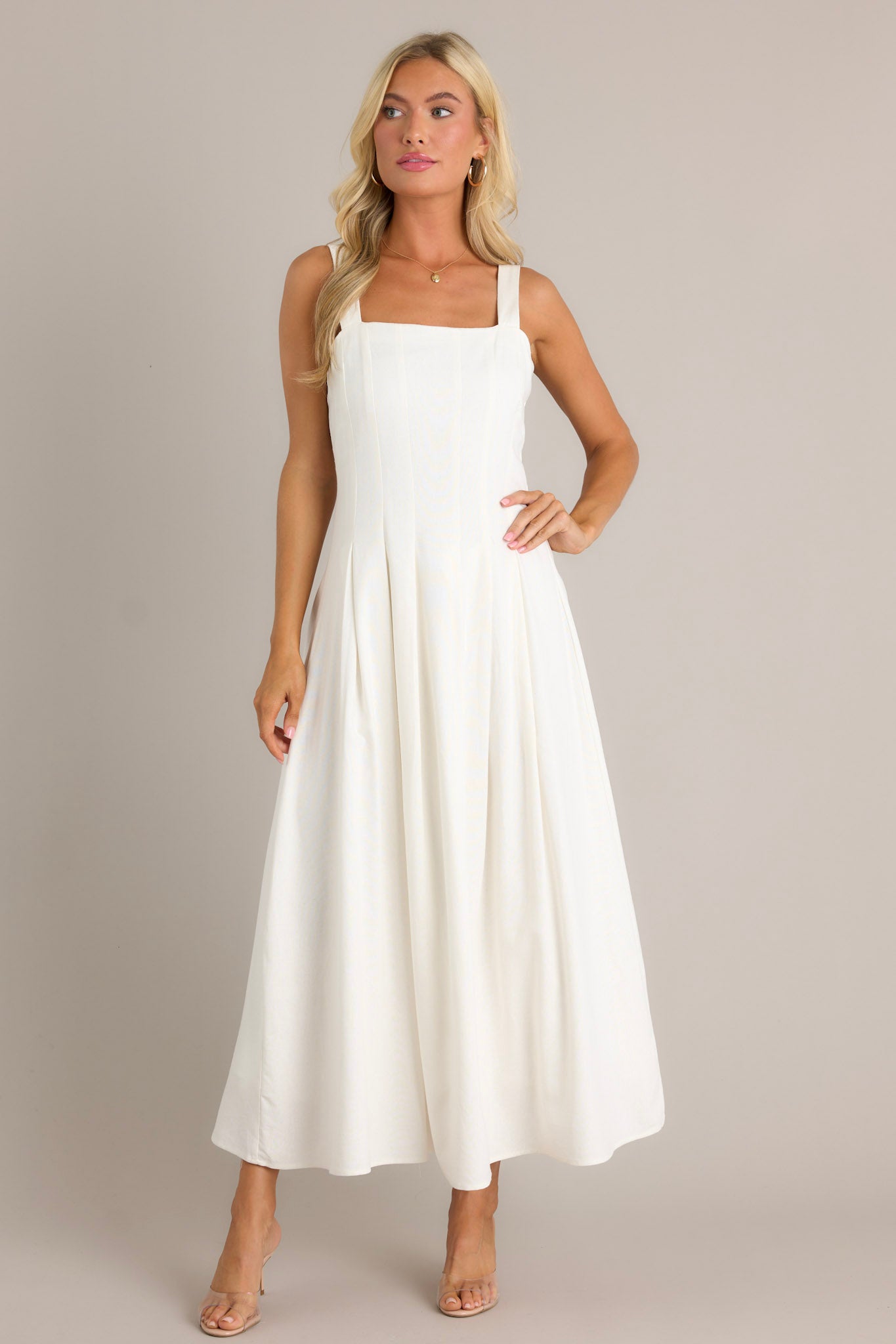 Full length view of an ivory dress featuring a square neckline, back smock insert, a discrete back zipper, a sleeveless design, and a flowing silhouette