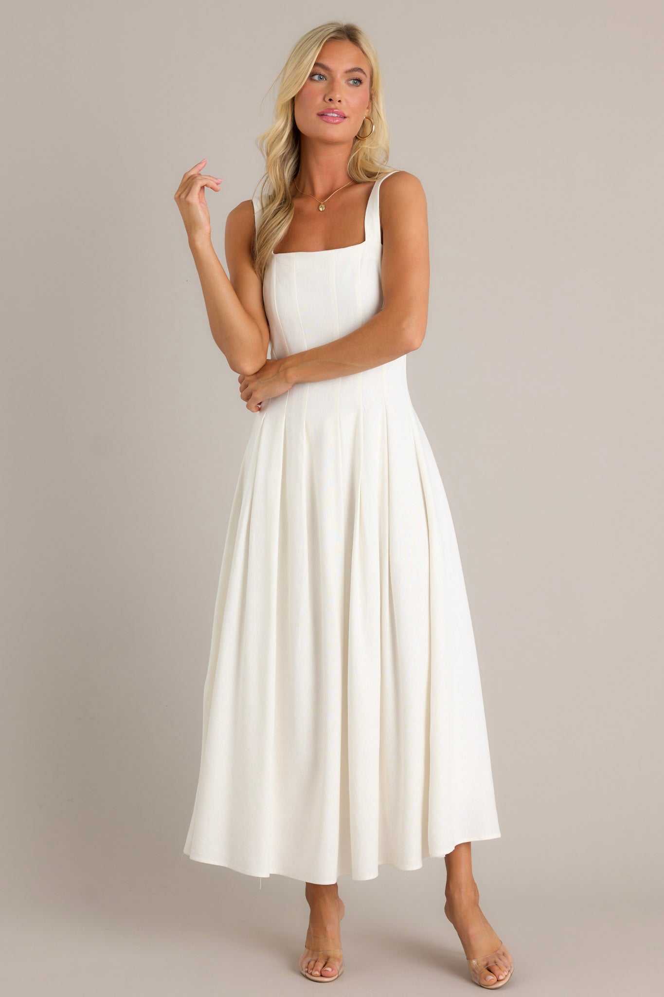 Front view of an ivory dress featuring a square neckline, a back smock insert, a discrete back zipper, a sleeveless design, and a flowing silhouette.