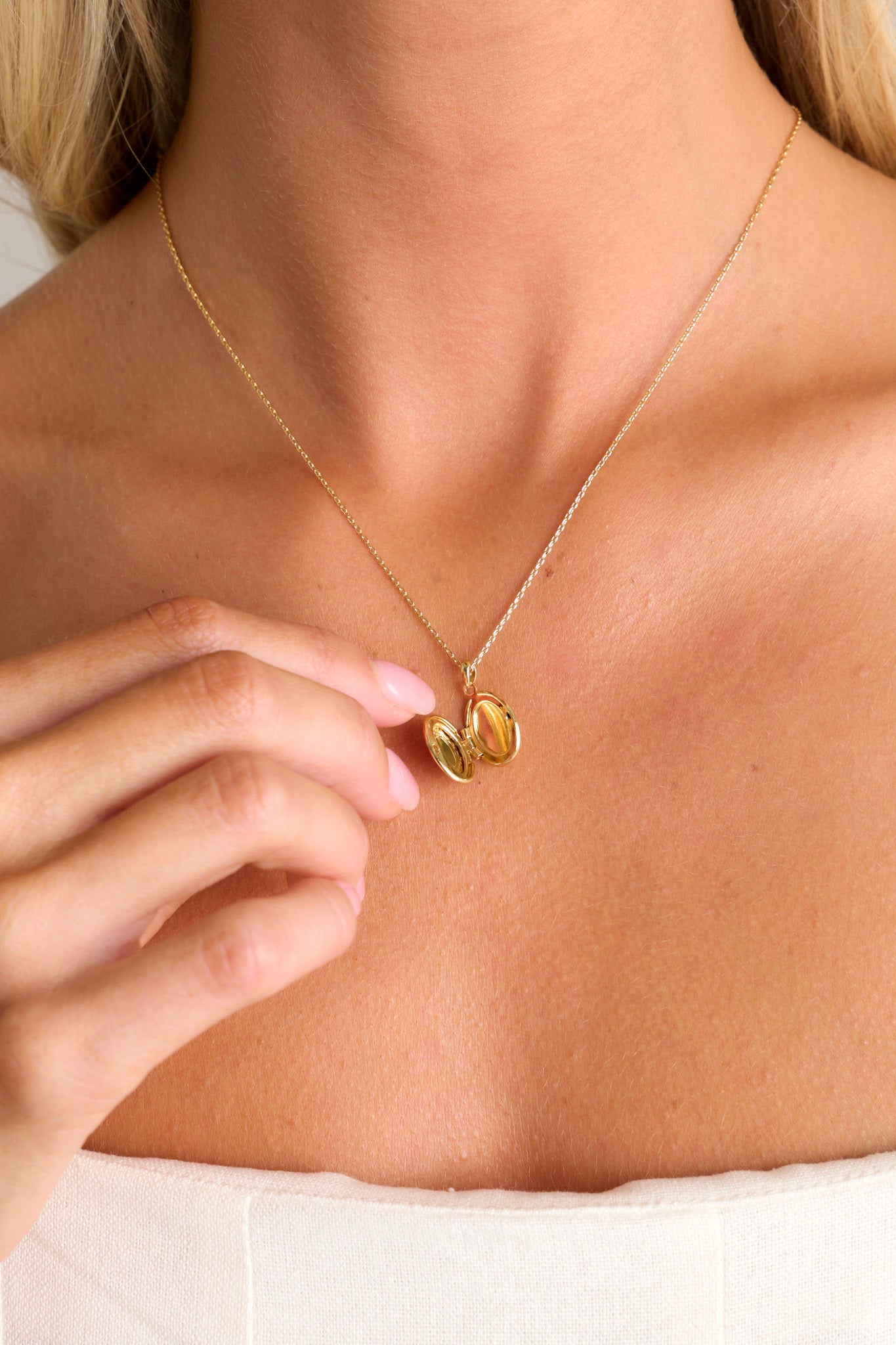 Open view of this gold locket that  features gold hardware, an oval locket, and an adjustable length.