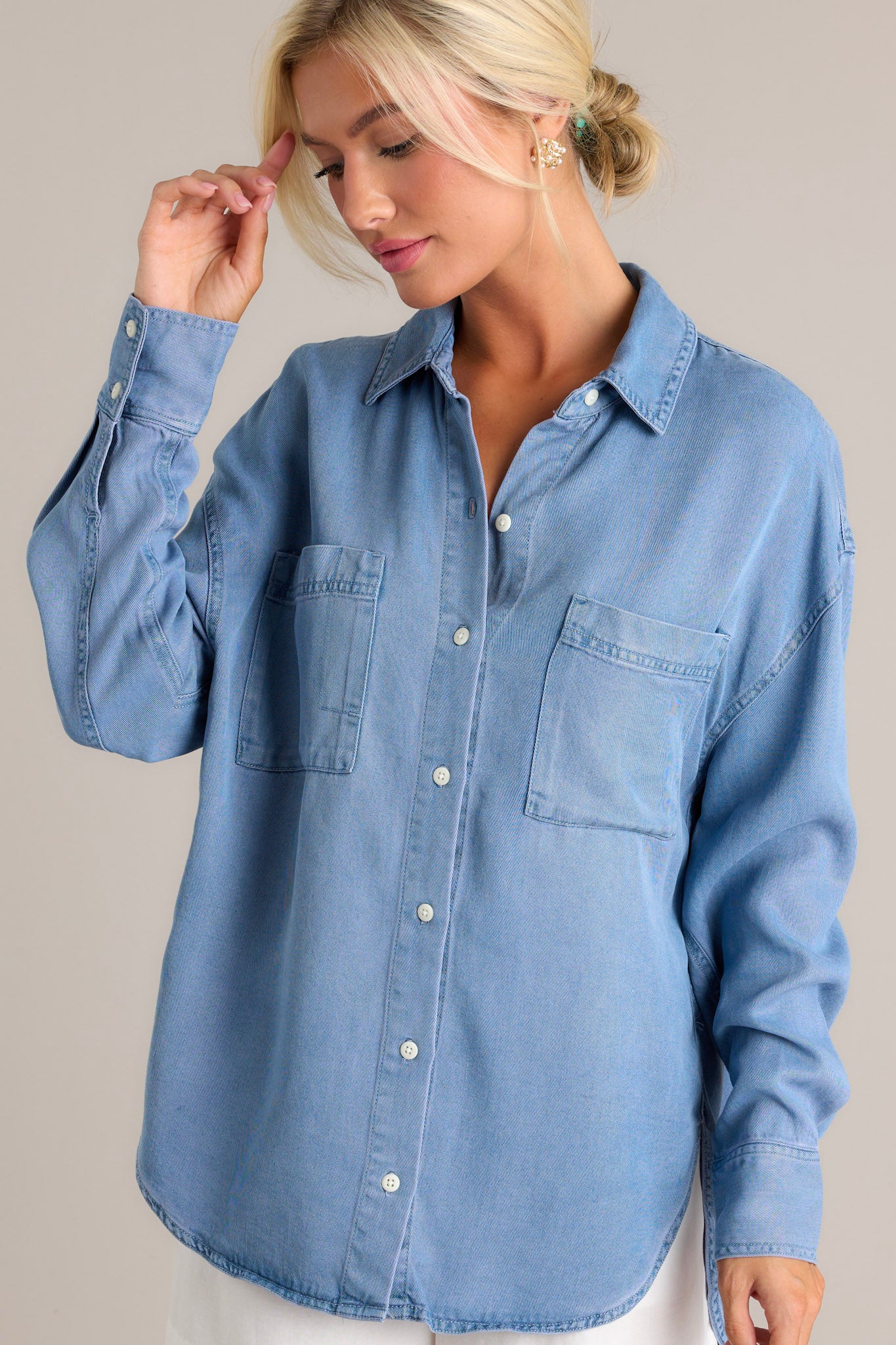 Front angled view of the chambray top featuring a collared neckline, functional button front, two chest pockets, a drop cut style, and long sleeves