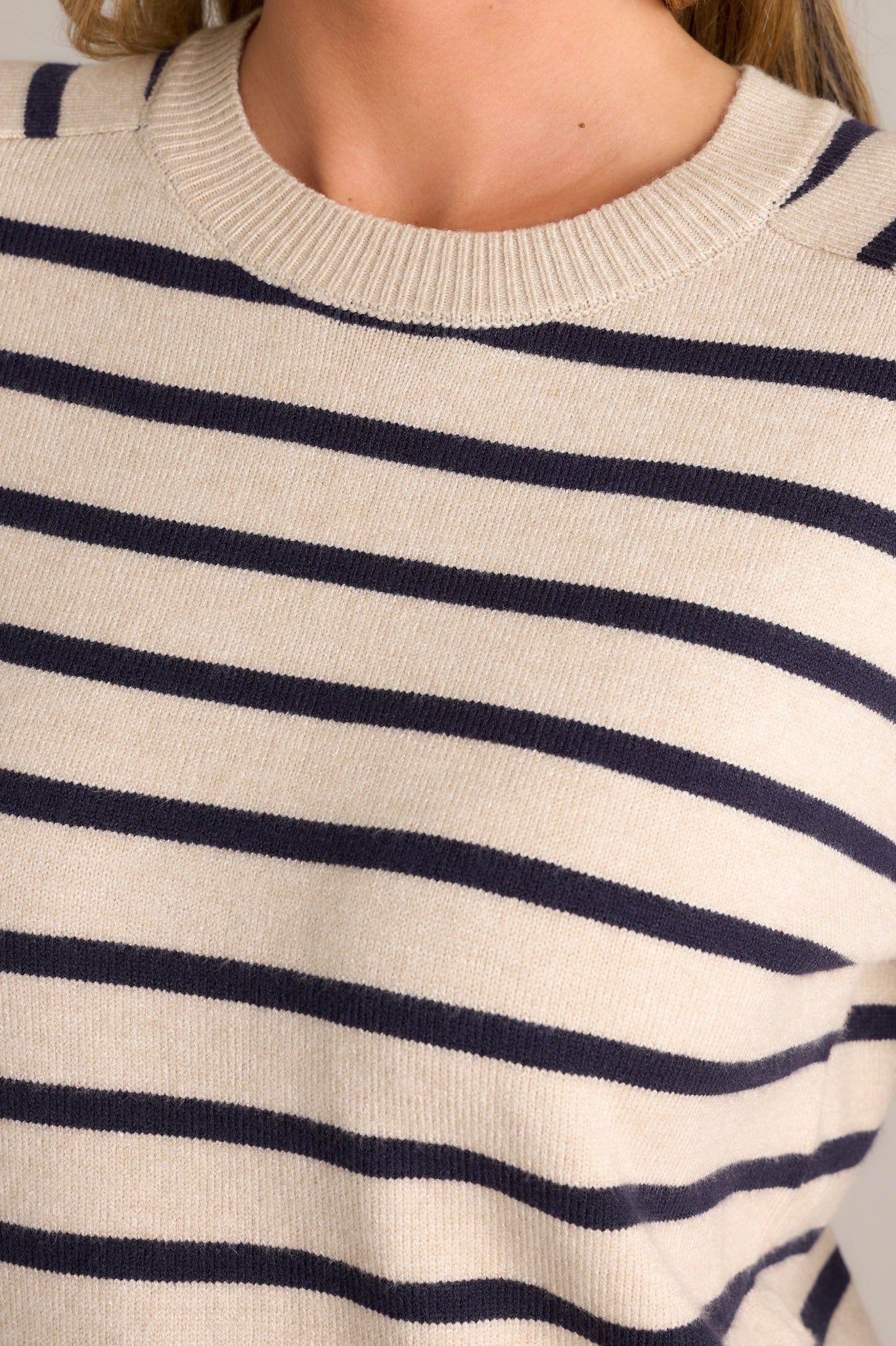 Close-up of a beige long sleeve showing the ribbed neckline, horizontal stripe pattern, soft sweater fabric, and cuffed long sleeves.