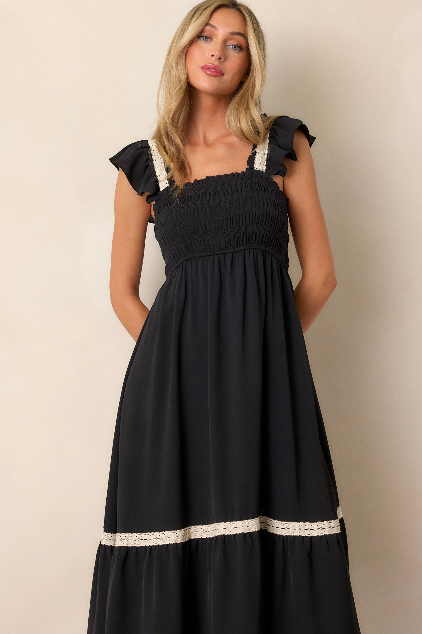 Close-up of the black dress focusing on the smocked bodice, square neckline, and the intricate white lace detailing on the short ruffle sleeves and tier trim.