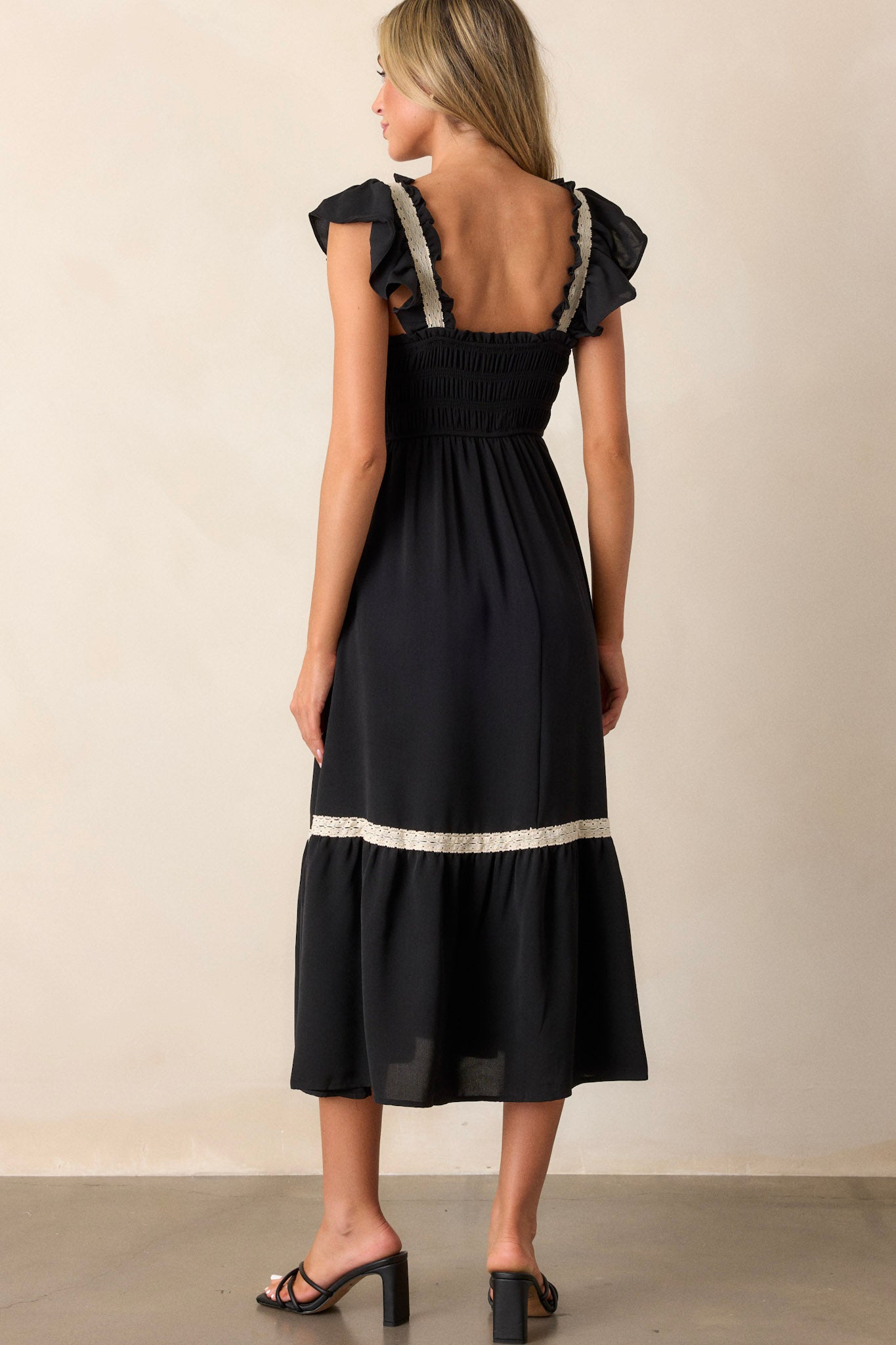 Back view of the black dress highlighting the smocked bodice, tiered design, and the short ruffle sleeves with white lace trim.