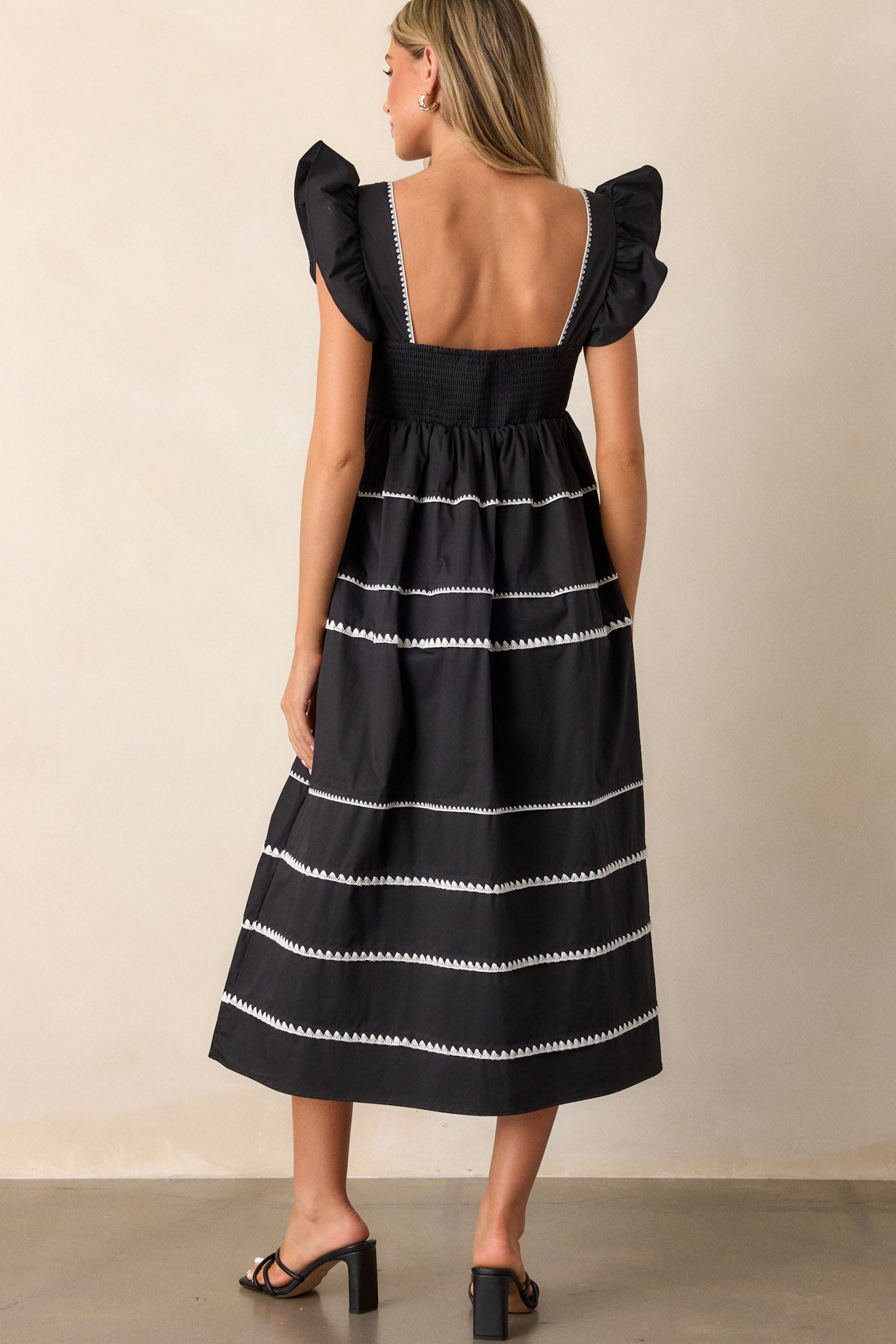 Back view of the black dress highlighting the smocked back, the multiple tiers, and a subtle view of the ruffle cap sleeves and ric-rac detailing.