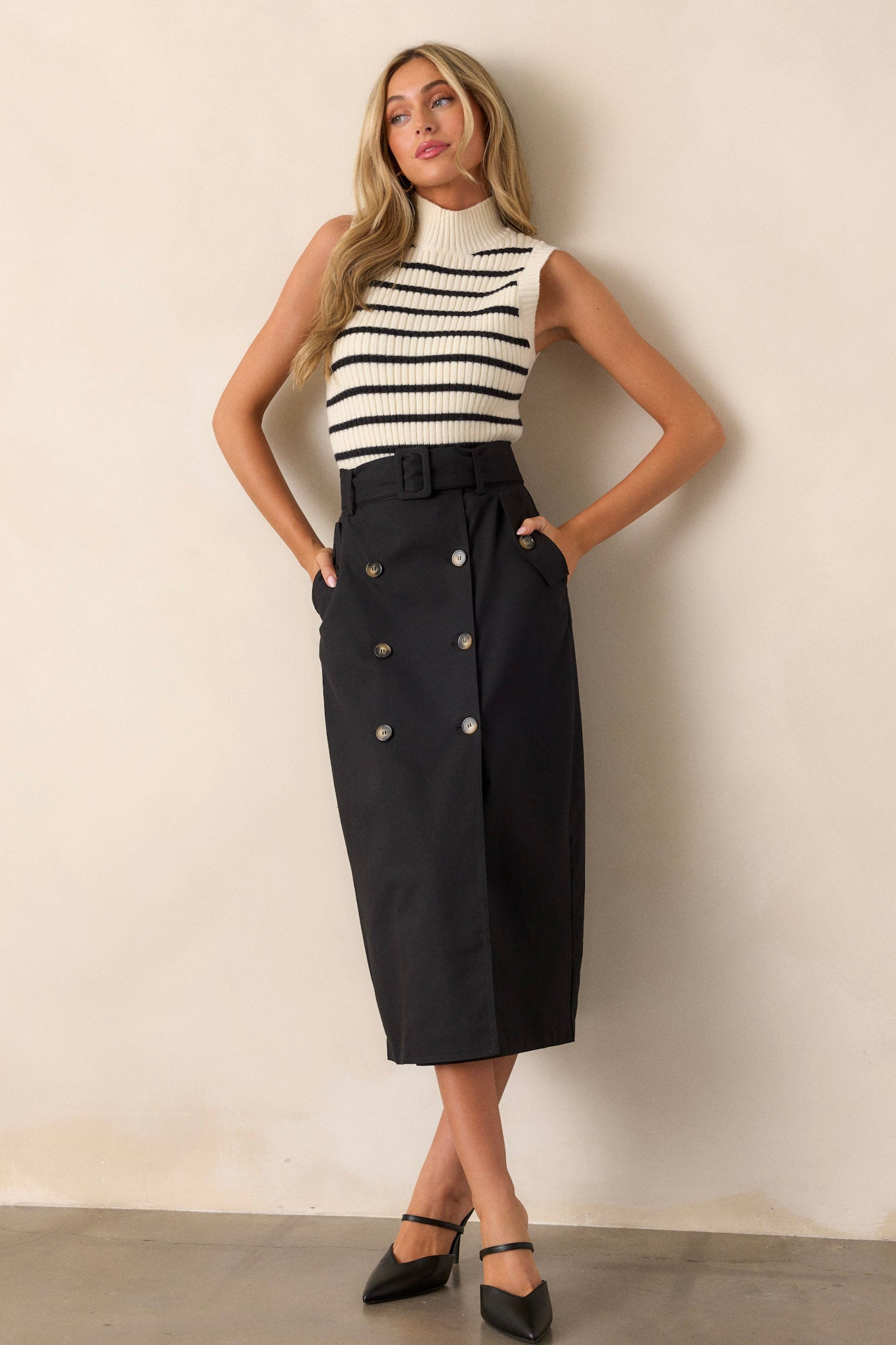 Full length view of a black maxi skirt featuring a high waisted design, an elastic waist insert, a square fabric belt, functional hip pockets, functional front buttons, and an open leg