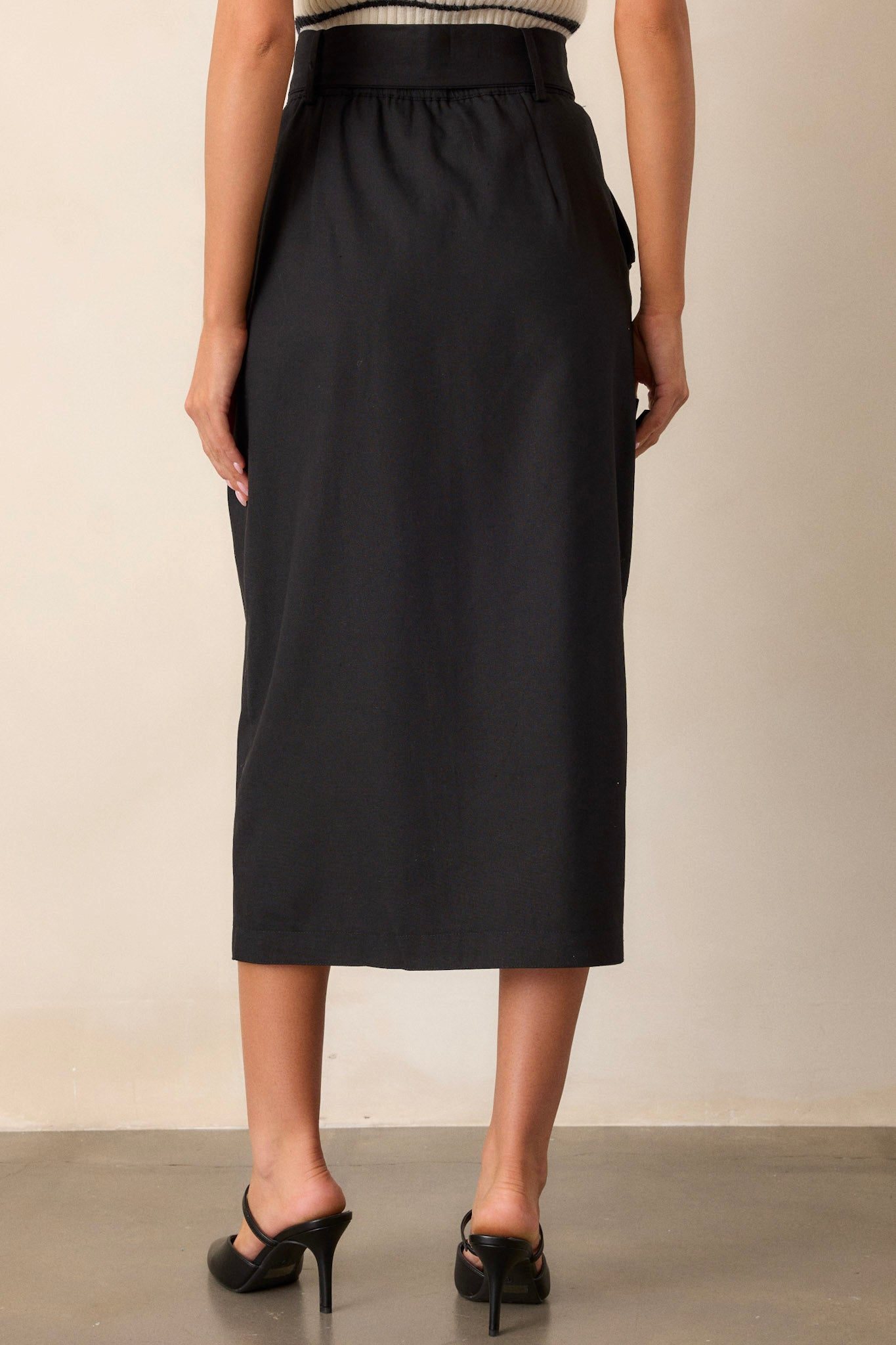 Back view of the black maxi skirt highlighting the elastic waist insert and the flowing silhouette, with a subtle view of the square fabric belt and functional hip pockets.