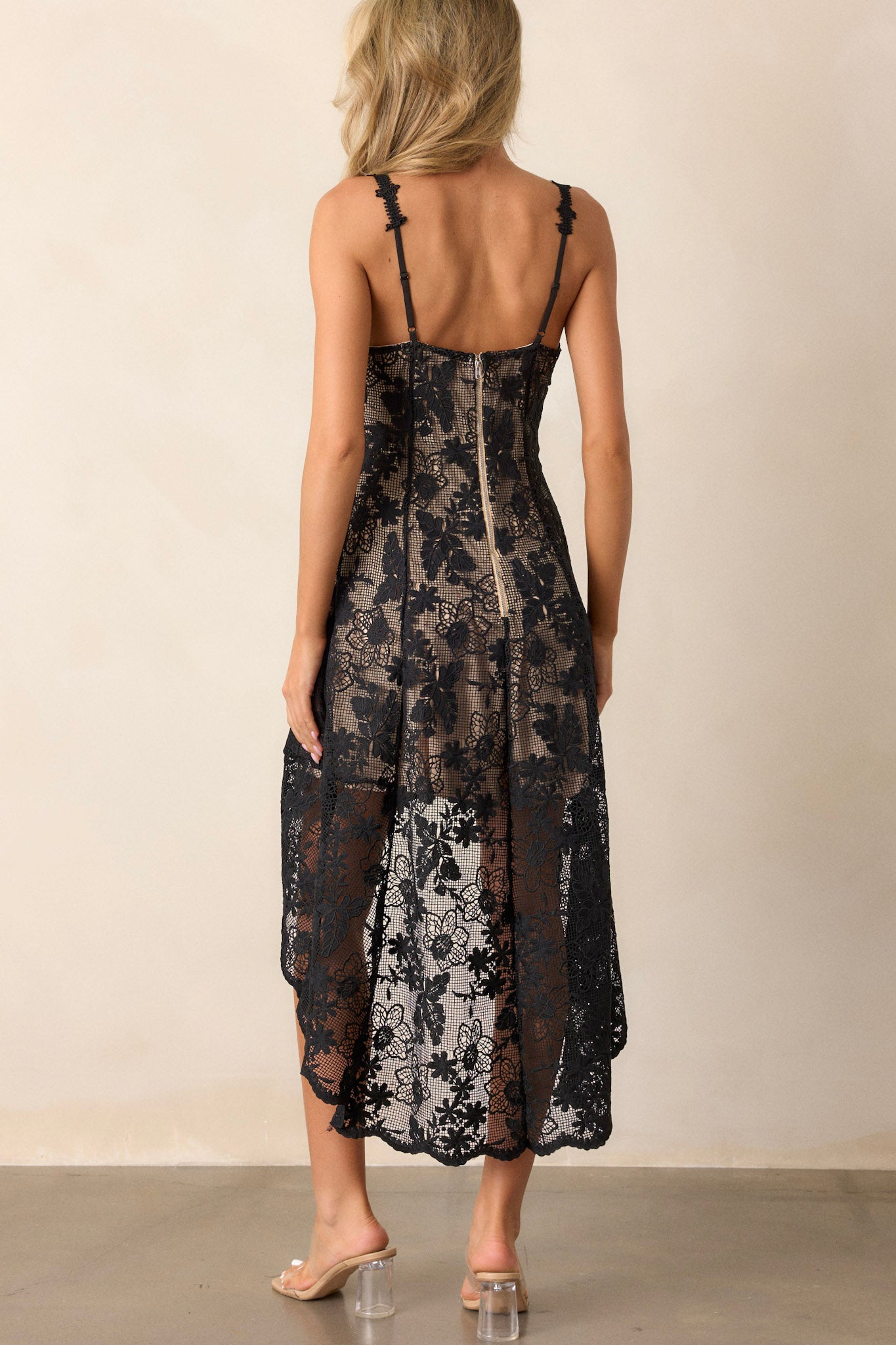 Back view of the black dress highlighting the functional zipper down the back, the delicate embroidered lace overlay, and the cascading high-low hemline.