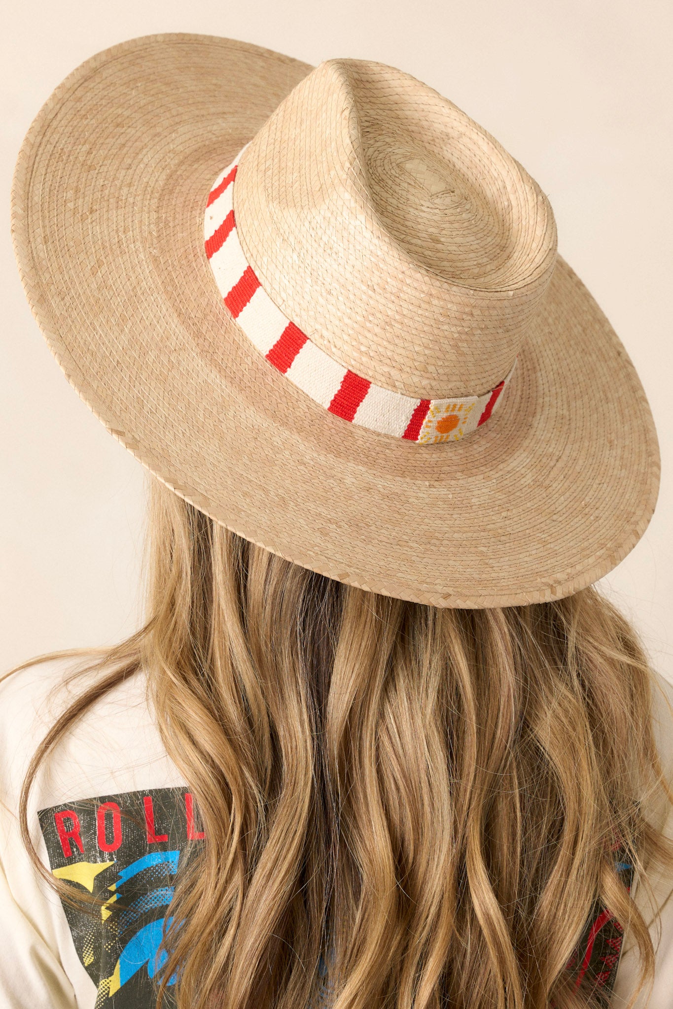 This hat features a woven red striped band, and is handmade with palm fronds.