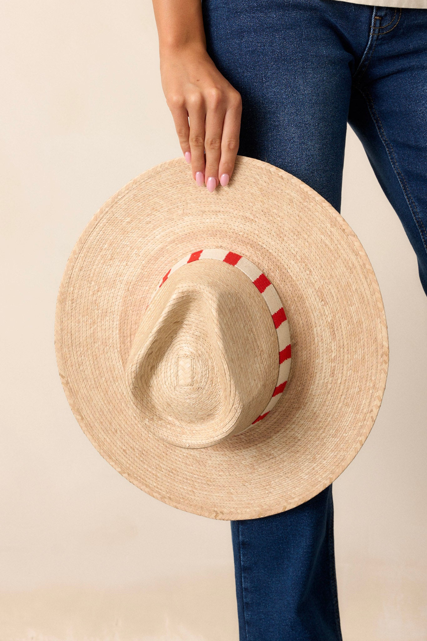 Hat featuring a woven red striped band, and is handmade with palm fronds.