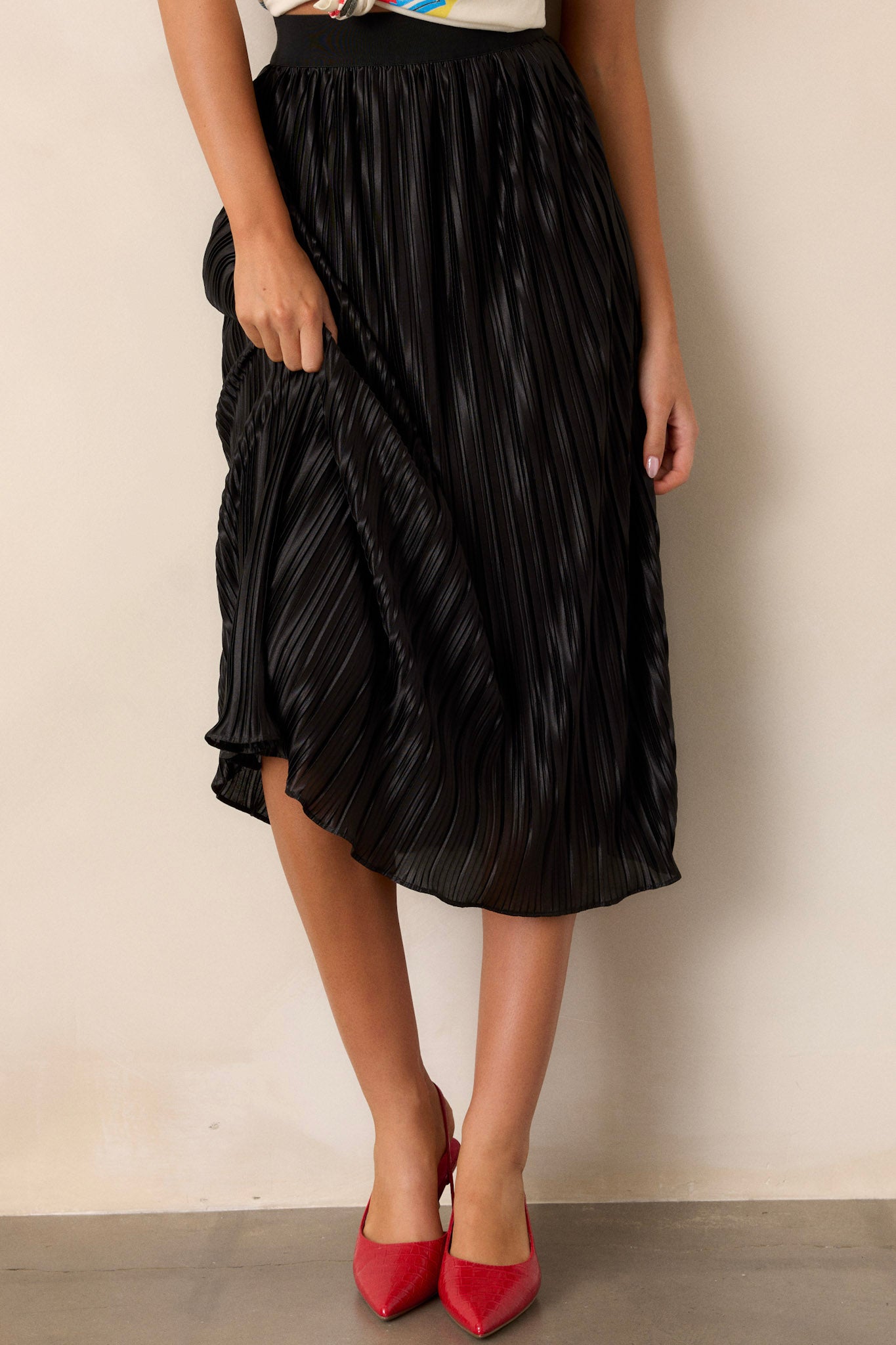 Black skirt featuring a high-waisted fit, an elastic waistband, shiny material, and a pleated design.