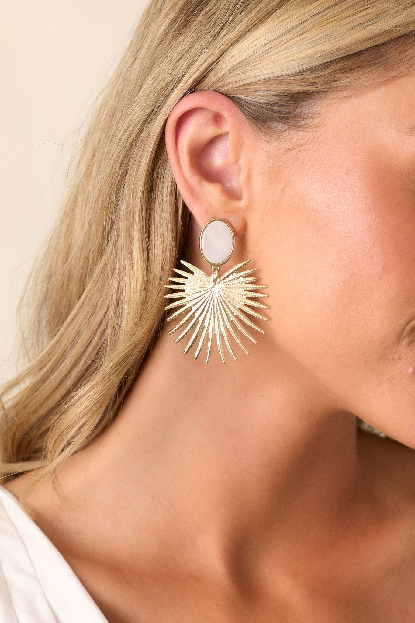 These gold earrings feature a faux opalescent stud, a gold statement drop, and secure post backings.