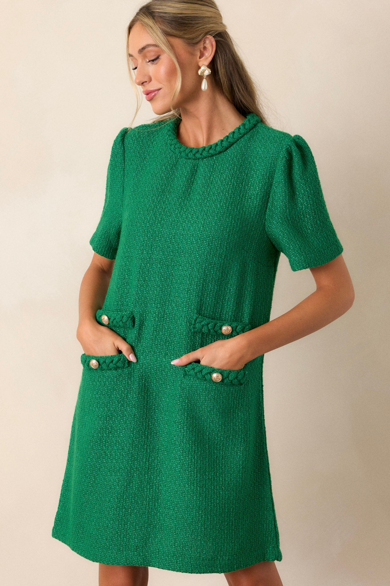 Angled view of the green mini dress showcasing the braided round neckline, gold accent buttons, functional front pockets, and the tweed material