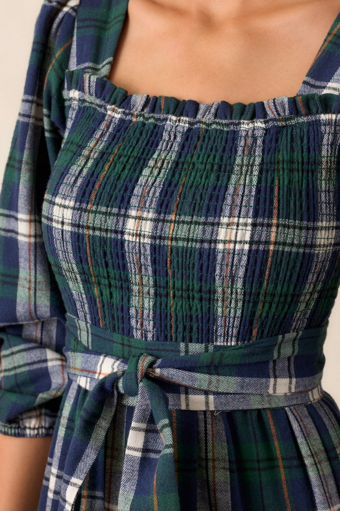 Close-up of the dress focusing on the square neckline, the fully smocked bust section, the self-tie belt at the waist, and the elastic cuffs on the long sleeves.