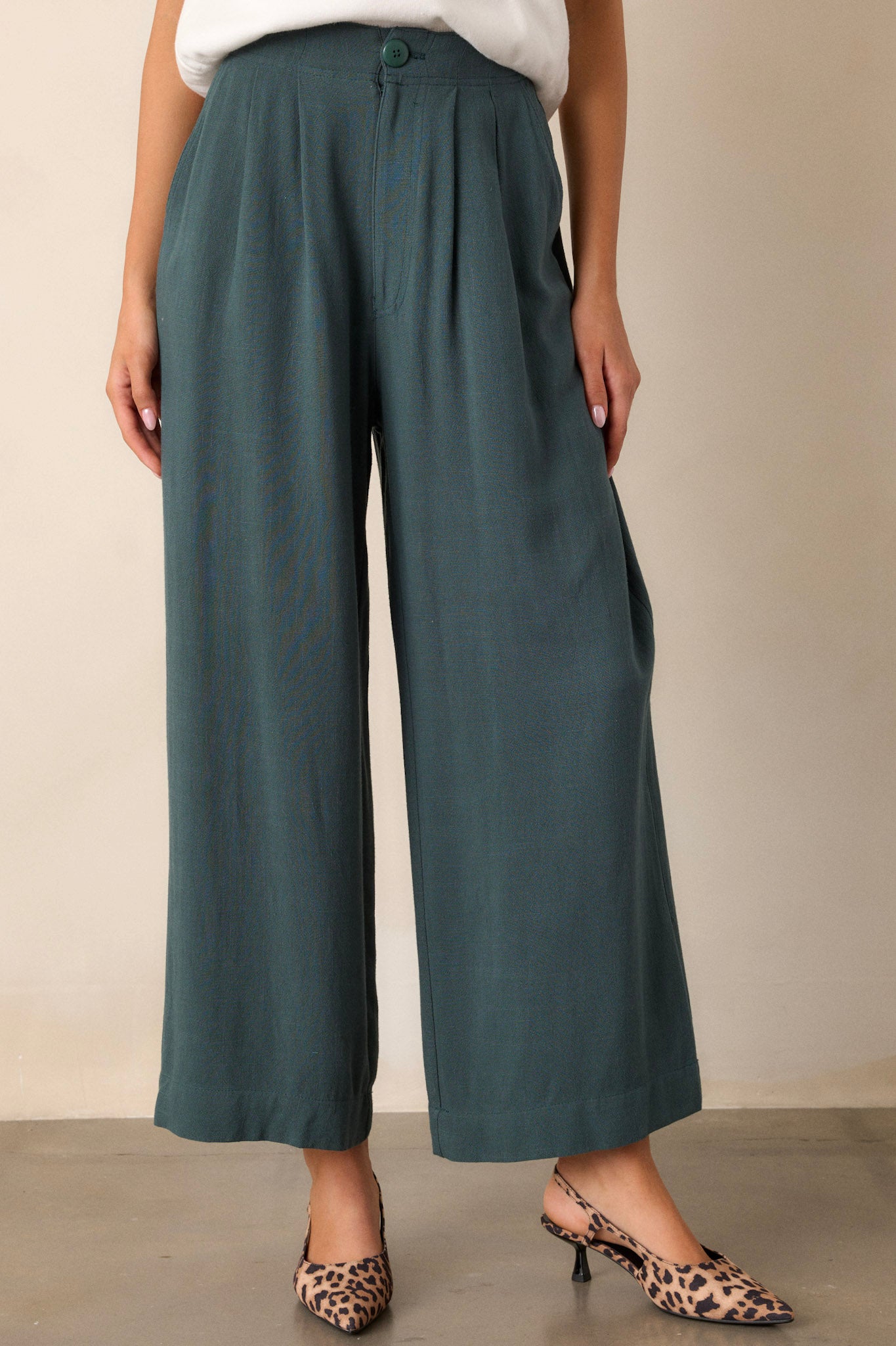 Full length view of green pants featuring an elastic waist insert, button zipper closure, functional hip pockets, and a straight leg design