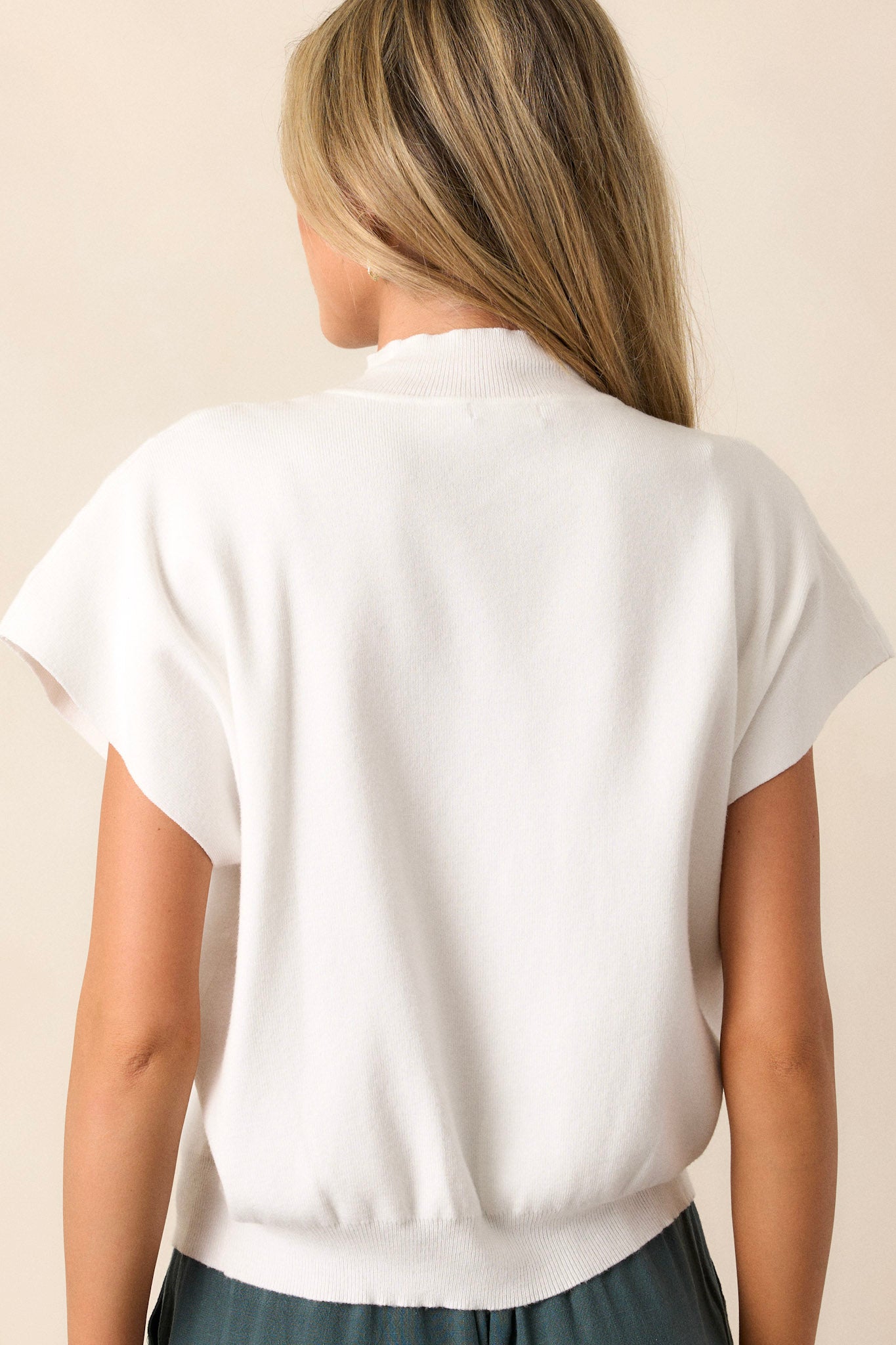 Back view of an ivory sweater top highlighting the ribbed high neckline, short sleeves, and ribbed hemline.