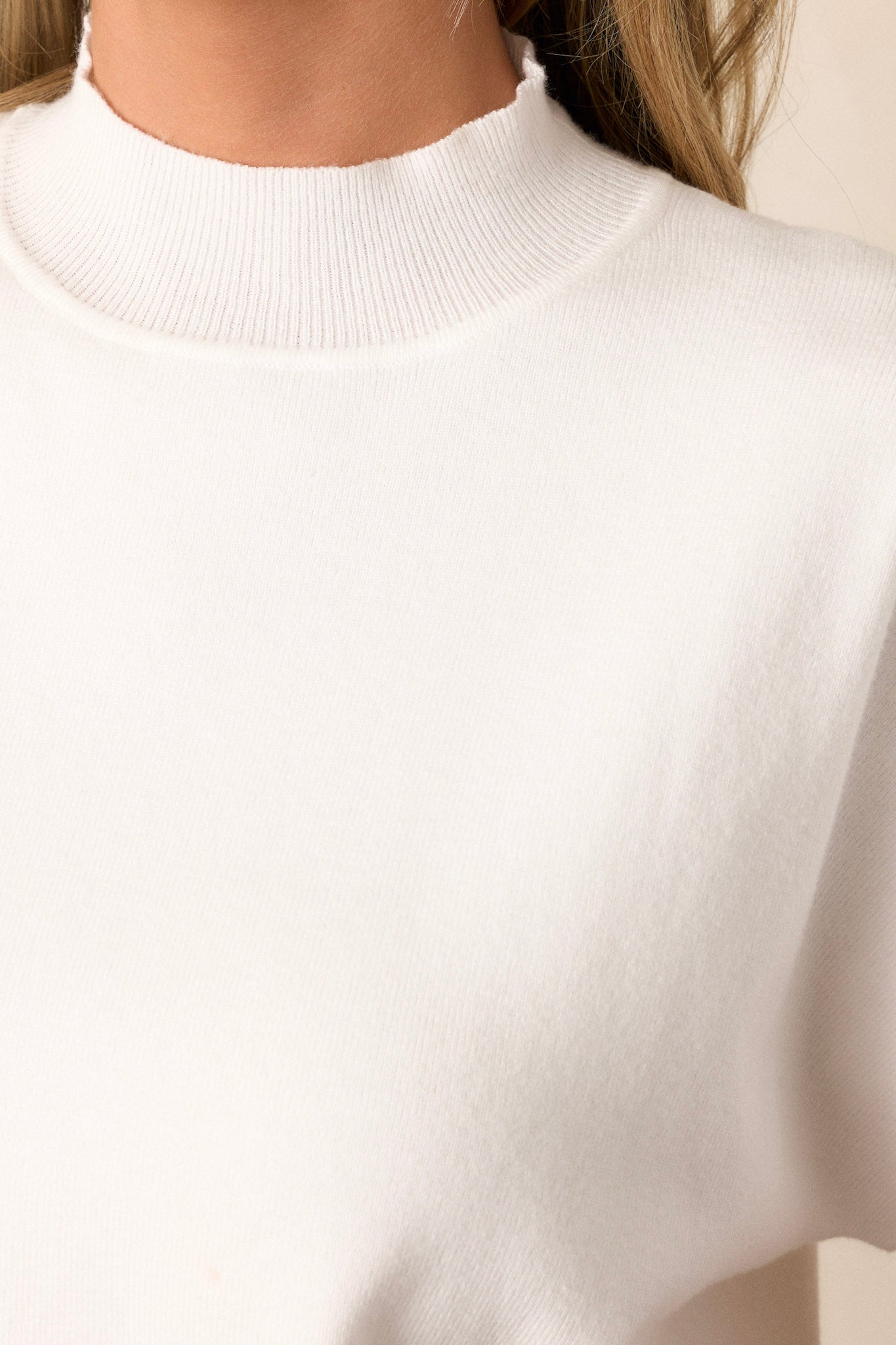 Close-up of the ivory sweater top showing the ribbed high neckline, the texture of the soft sweater fabric, and the ribbed hemline.