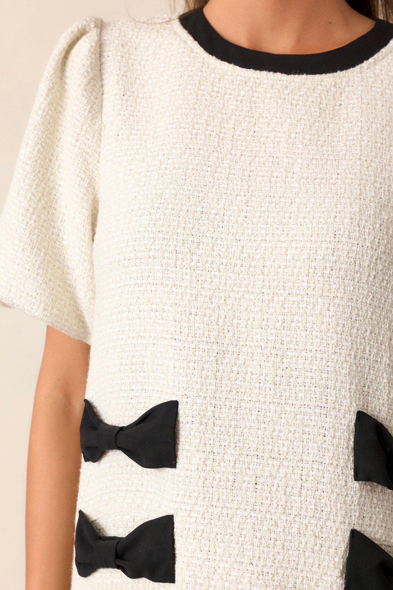 Close-up of the ivory tweed dress focusing on the black bow detailing on the hips, the functional hip pockets, and the texture of the tweed fabric.