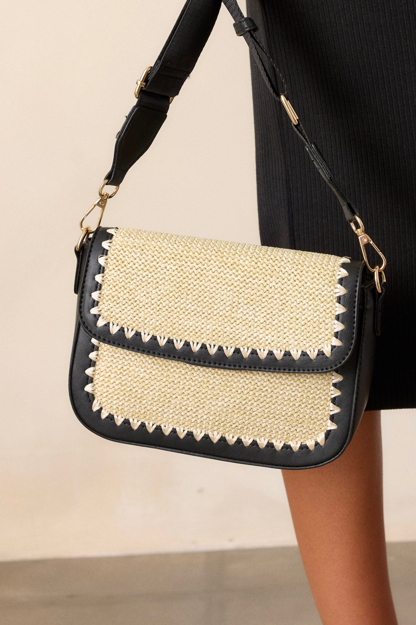 Close-up of this black woven handbag that features a magnetic flap closure, two inside pockets, gold hardware, and an optional crossbody strap.