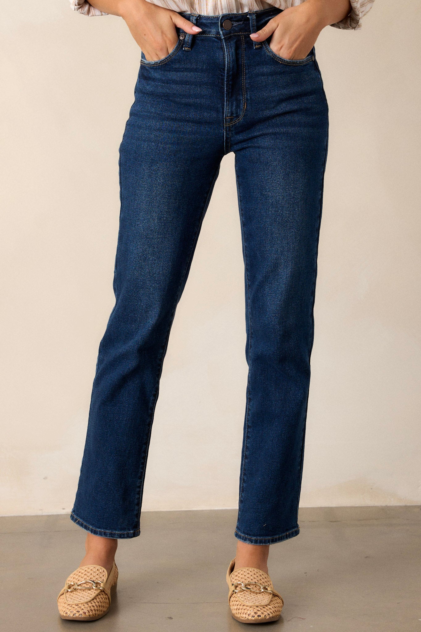 Front view of dark wash jeans featuring a high waisted design, a button and zipper closure, functional front pockets, and a straight leg.