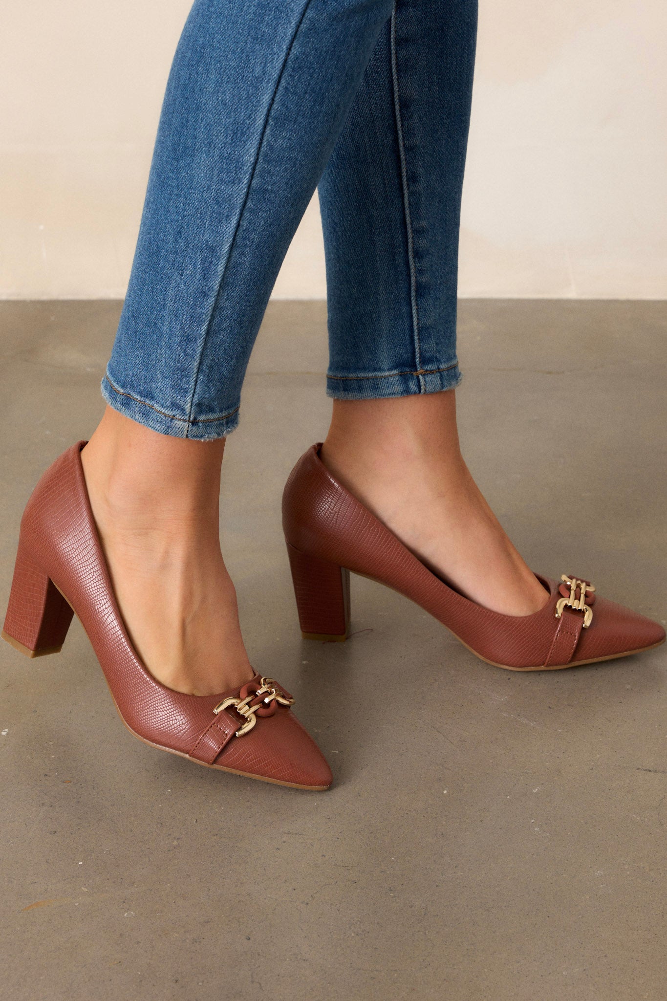 Angled view of these brown heels that feature a crocodile pattern, block heel, gold hardware, and a pointed toe.