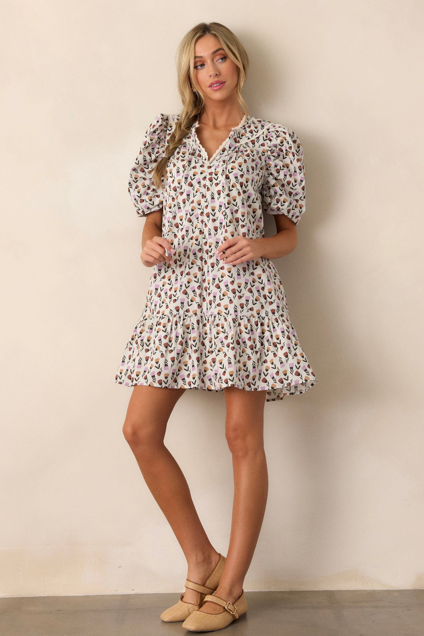 Full length view of the ivory floral dress featuring a lace trim v-neckline, a multi-color tulip pattern, functional hip pockets, a tiered design, and short puff sleeves with lace trim