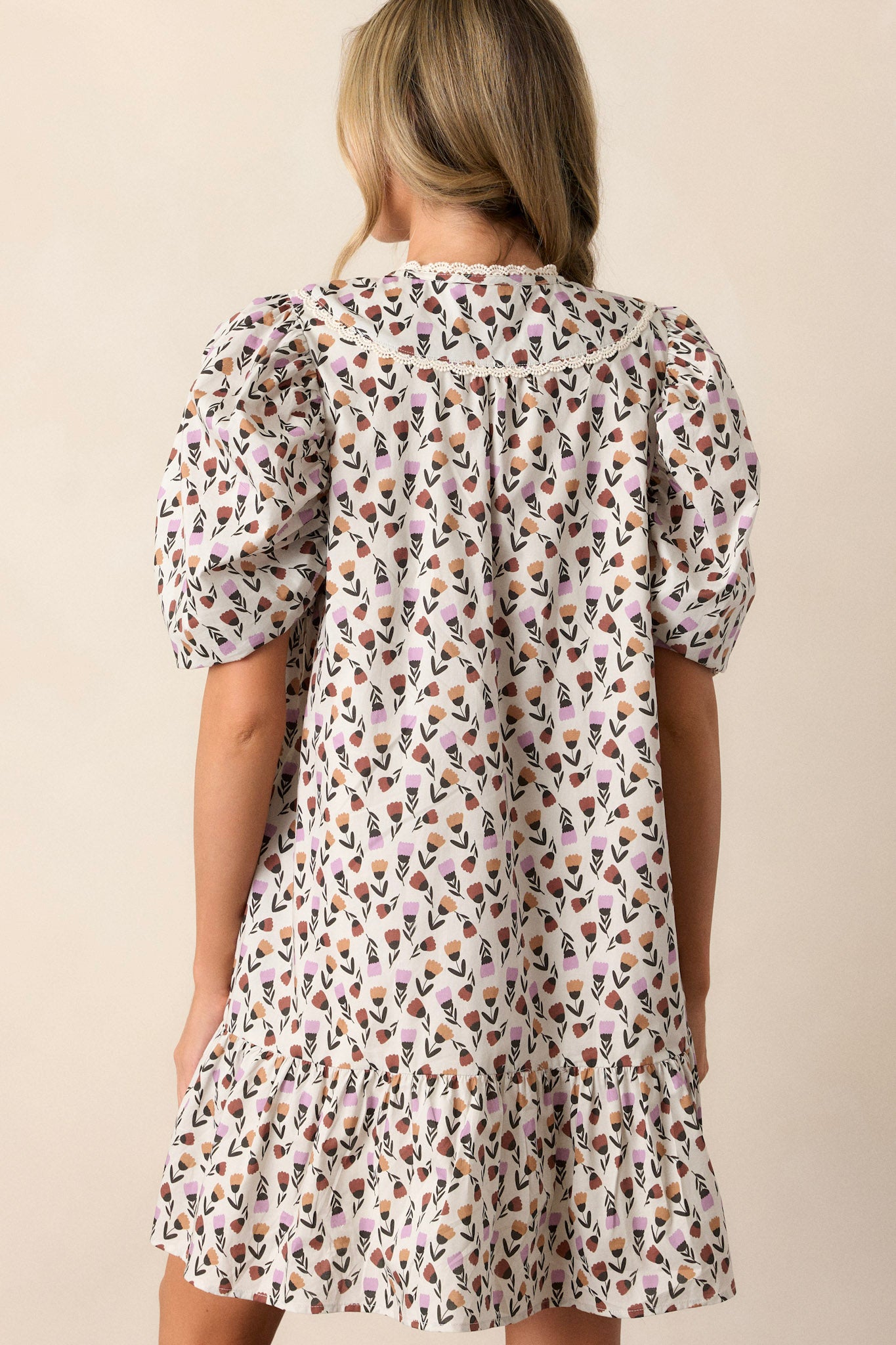 Back view of the ivory floral dress highlighting the tiered design and the flow of the fabric, along with the short puff sleeves with lace trim.