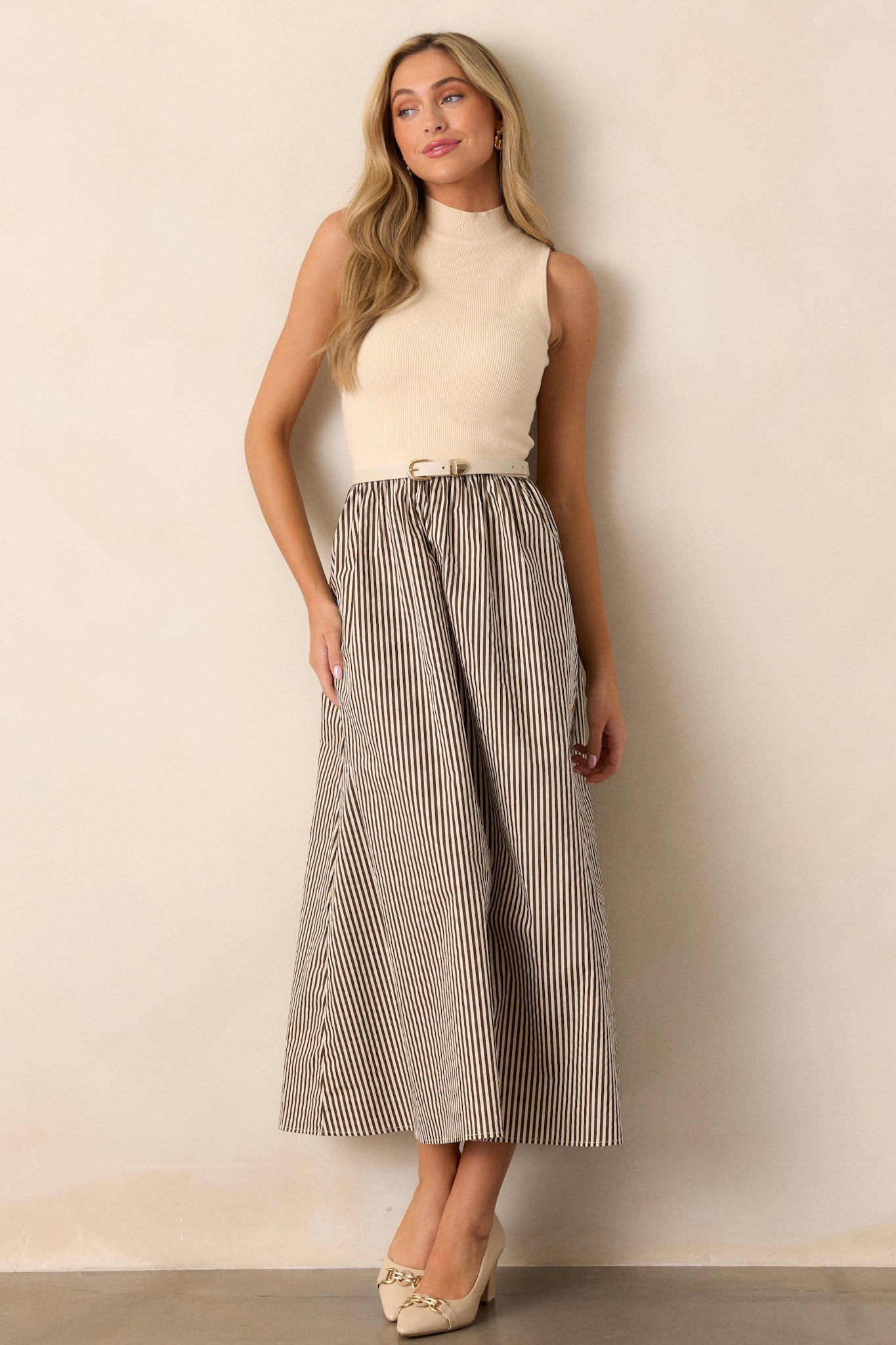 Full length view of a beige dress featuring a mock neckline, a cozy ribbed fabric on the bodice, and a brown striped skirt