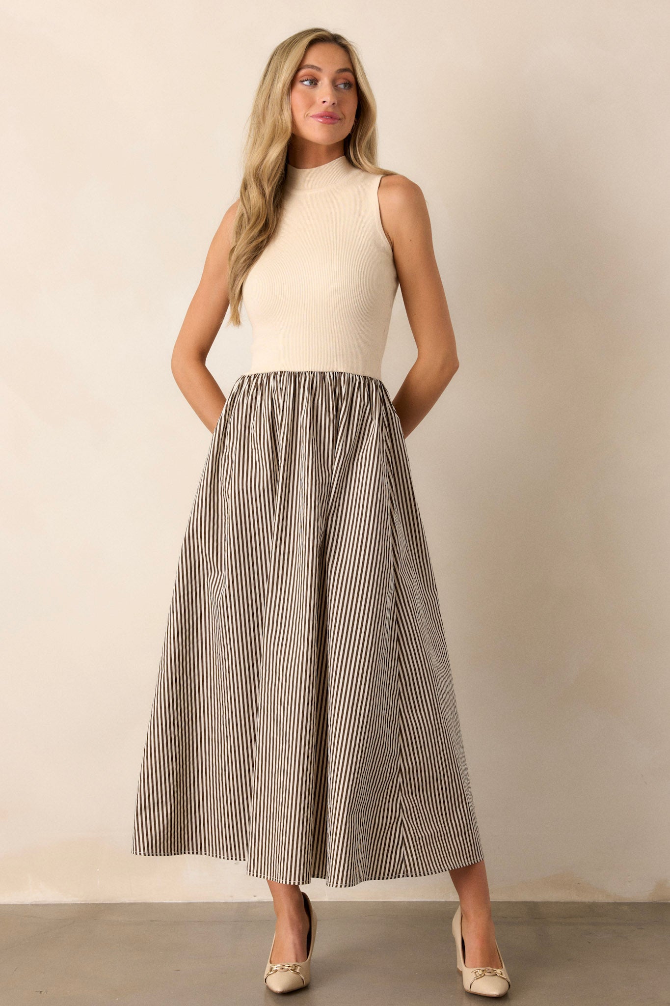 Front angled view of the beige dress featuring a mock neckline, ribbed bodice, and a brown striped skirt