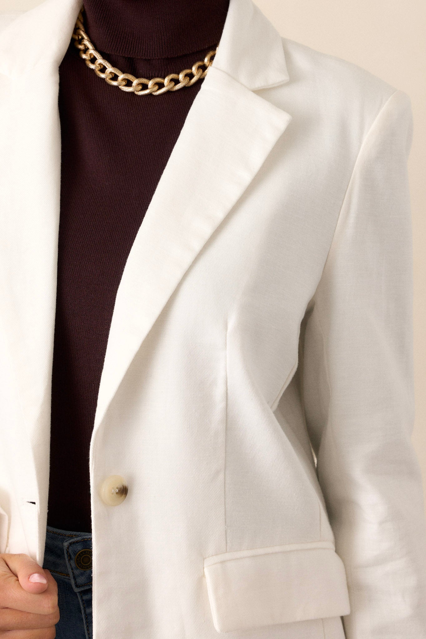 Close-up of the white blazer focusing on the collared neckline, functional half button front, and the texture of the fabric.