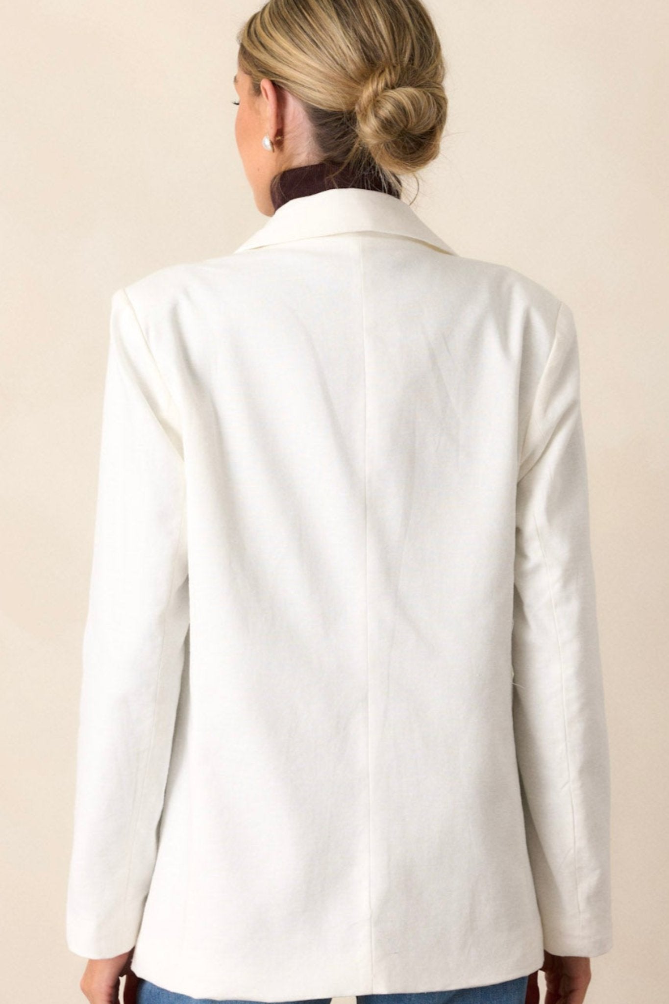 Back view of a white blazer highlighting the clean lines of the back, padded shoulders, and the full length of the long sleeves.