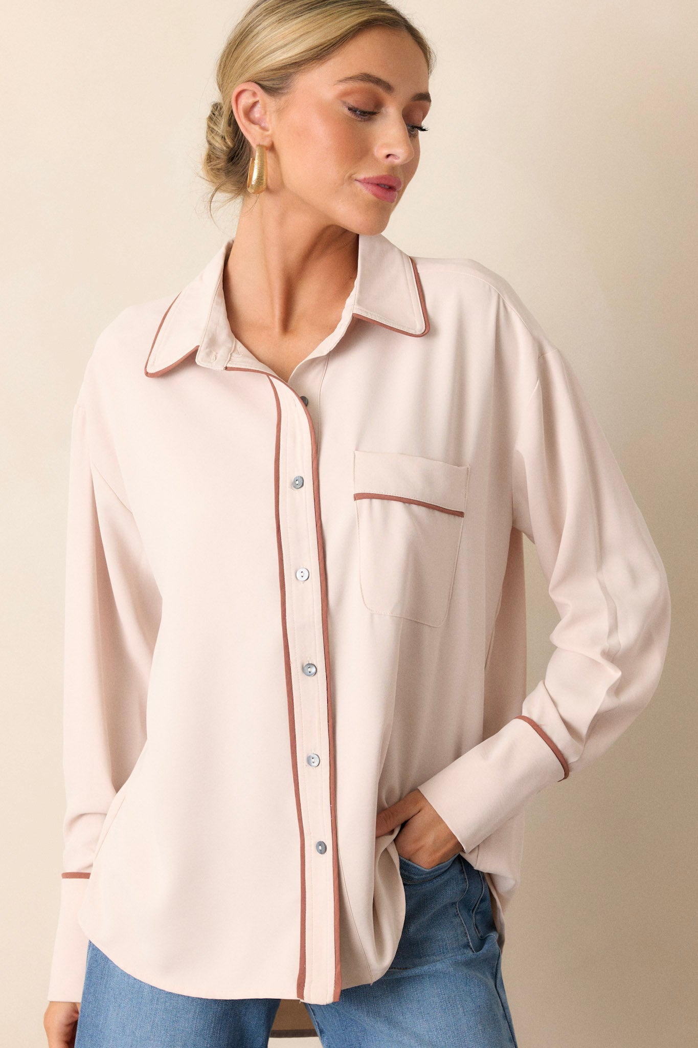 Front angled view of a beige top featuring a collared neckline, a functional breast pocket, a full button front, contrasting trim, and button-cuffed long sleeves