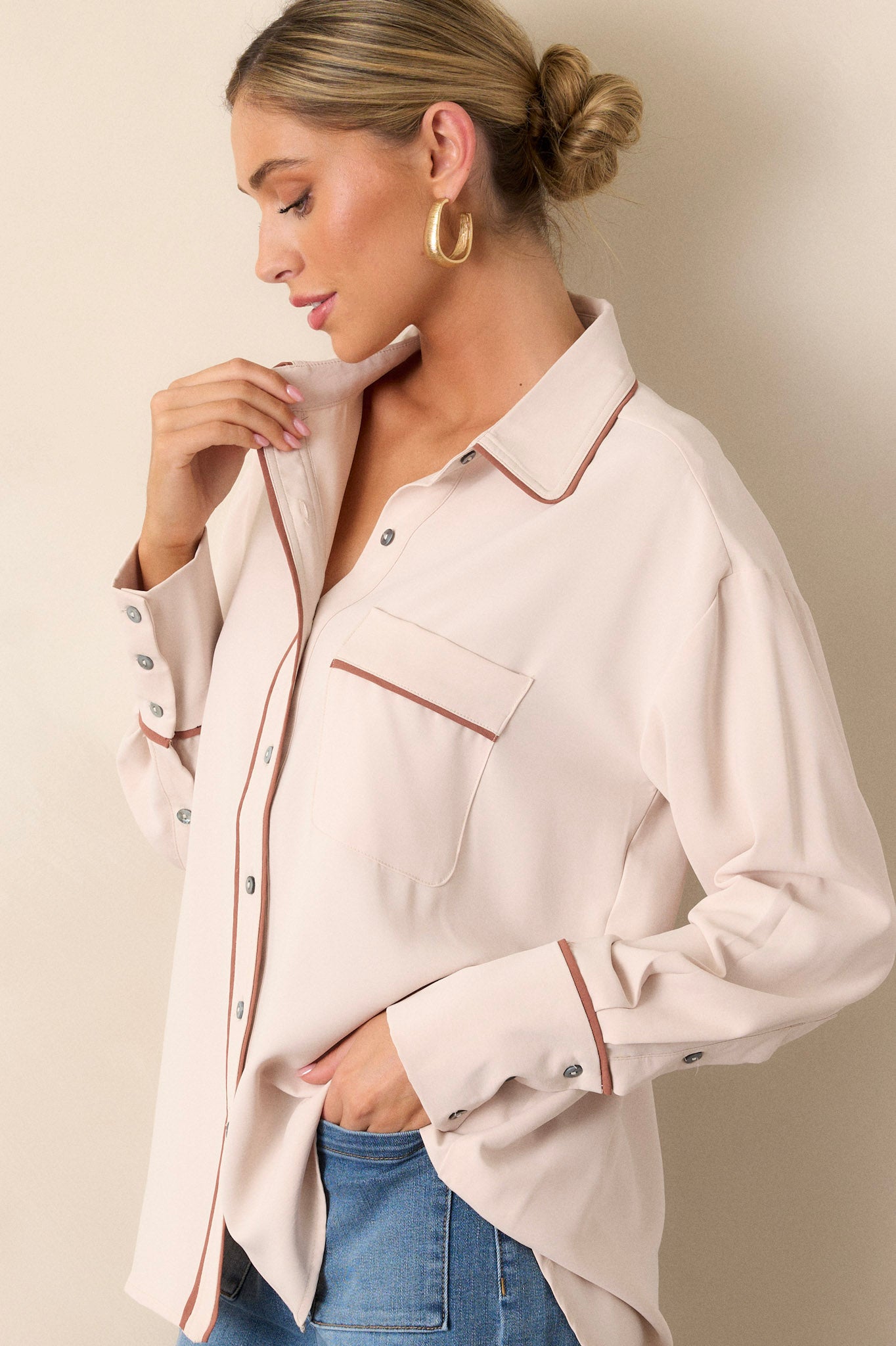 Side view of the beige top showcasing the collared neckline, functional breast pocket, and the contrasting trim on the button-cuffed long sleeves.