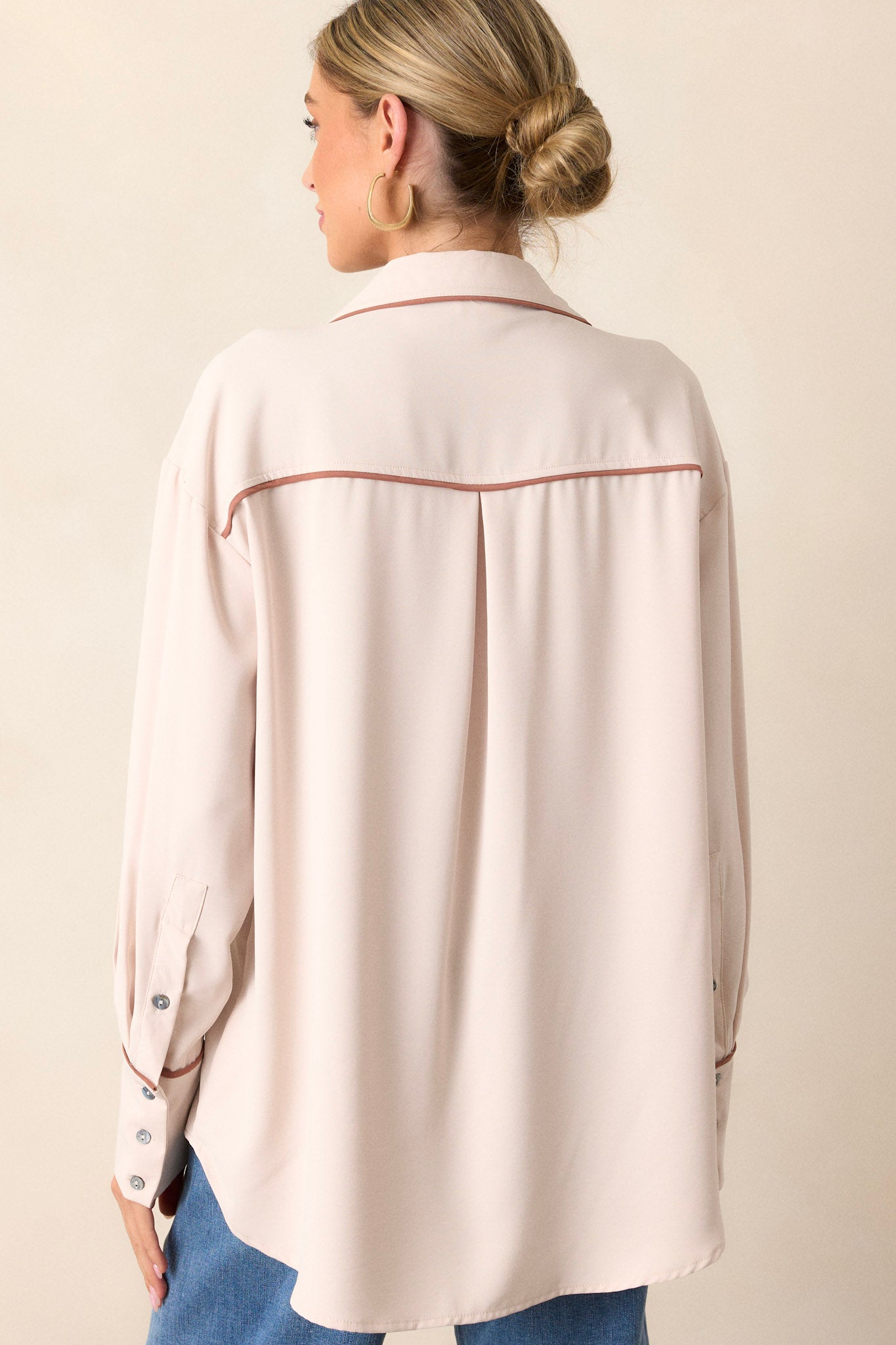 Back view of the beige top highlighting the button-cuffed long sleeves and the flow of the fabric.